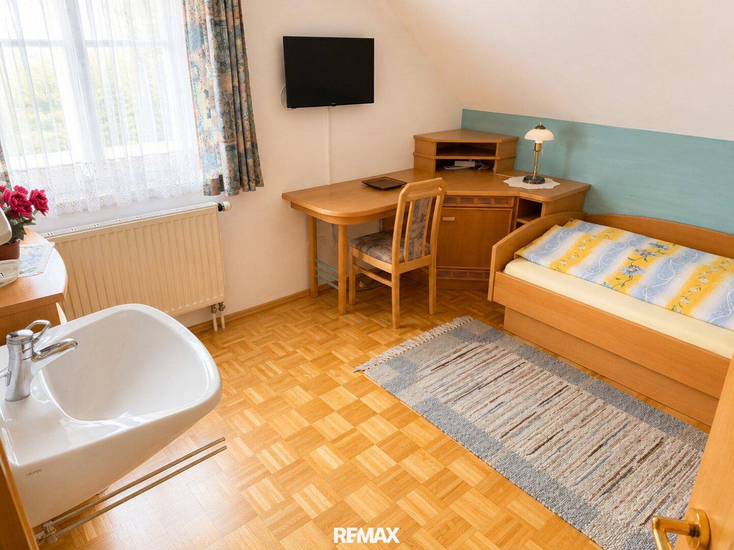 Einzelzimmer mit Holzboden, Schreibtisch und Fenster, ideal als Gäste- oder Kinderzimmer.