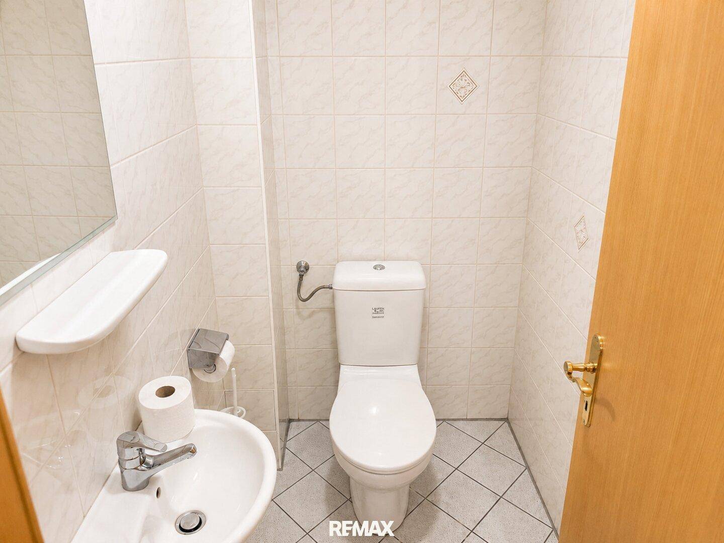 Separates WC mit Waschbecken und hellen Fliesen, funktional und sauber.