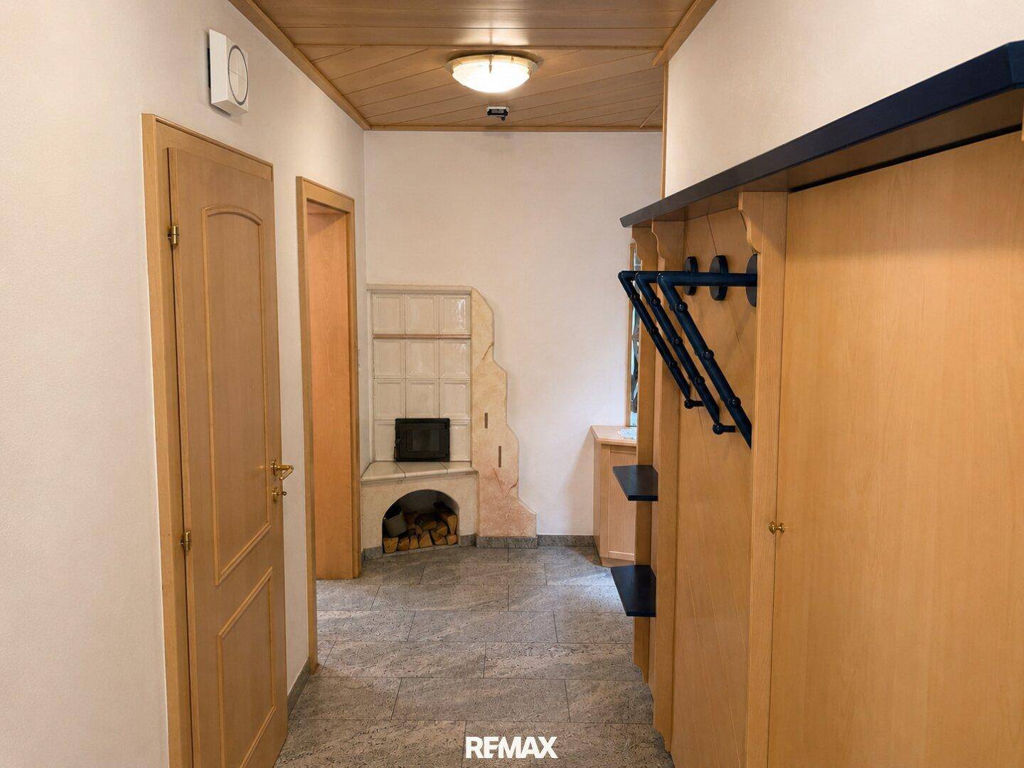 Heller Eingangsbereich mit Fliesenboden, Holzdecke und traditionellem Kachelofen.