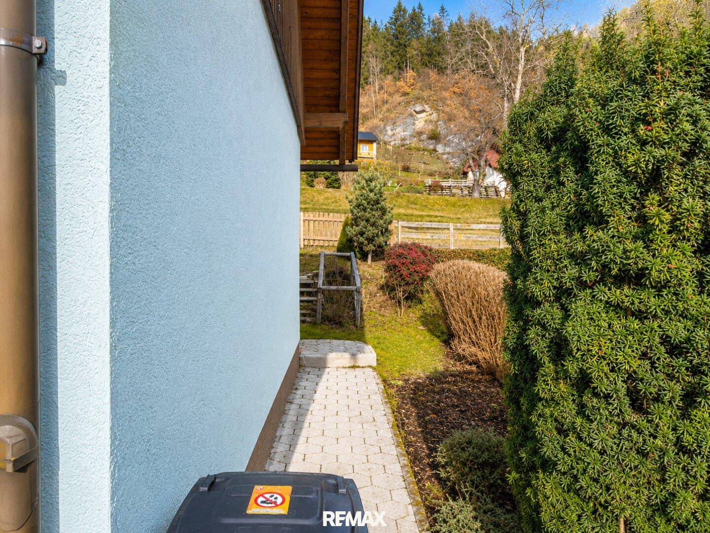 Seitenansicht des Hauses mit gepflastertem Weg und grüner Hecke.