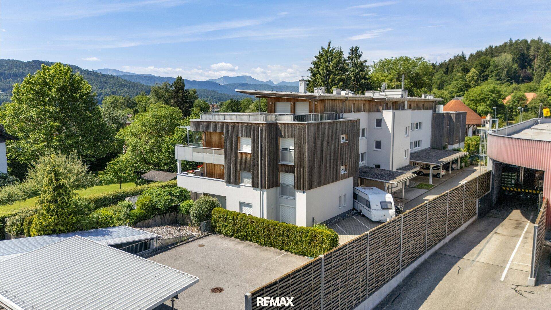 Moderne Wohnanlage mit Holzfassade, Balkonen und Bergblick in grüner Umgebung.