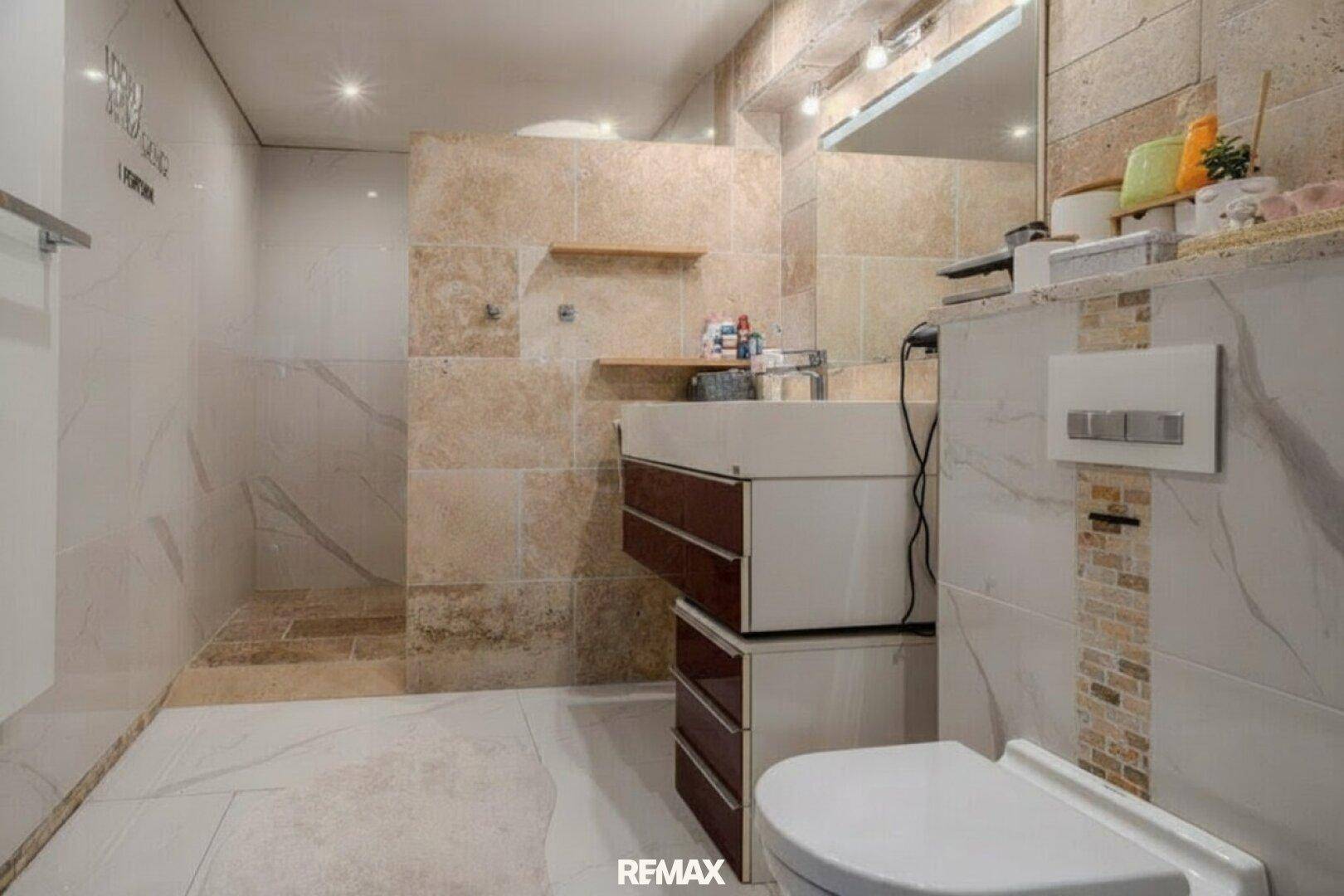 Modernes Badezimmer mit beigefarbenen Fliesen, begehbarer Dusche und Wand-WC.