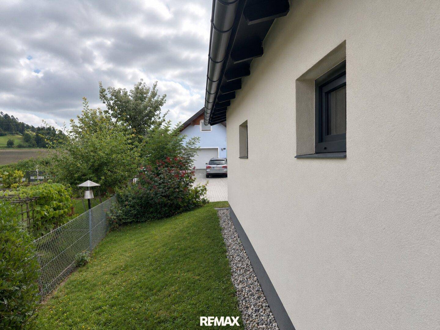 Seitenansicht des Hauses mit grünem Hang, Zaun und Blick auf die Umgebung.
