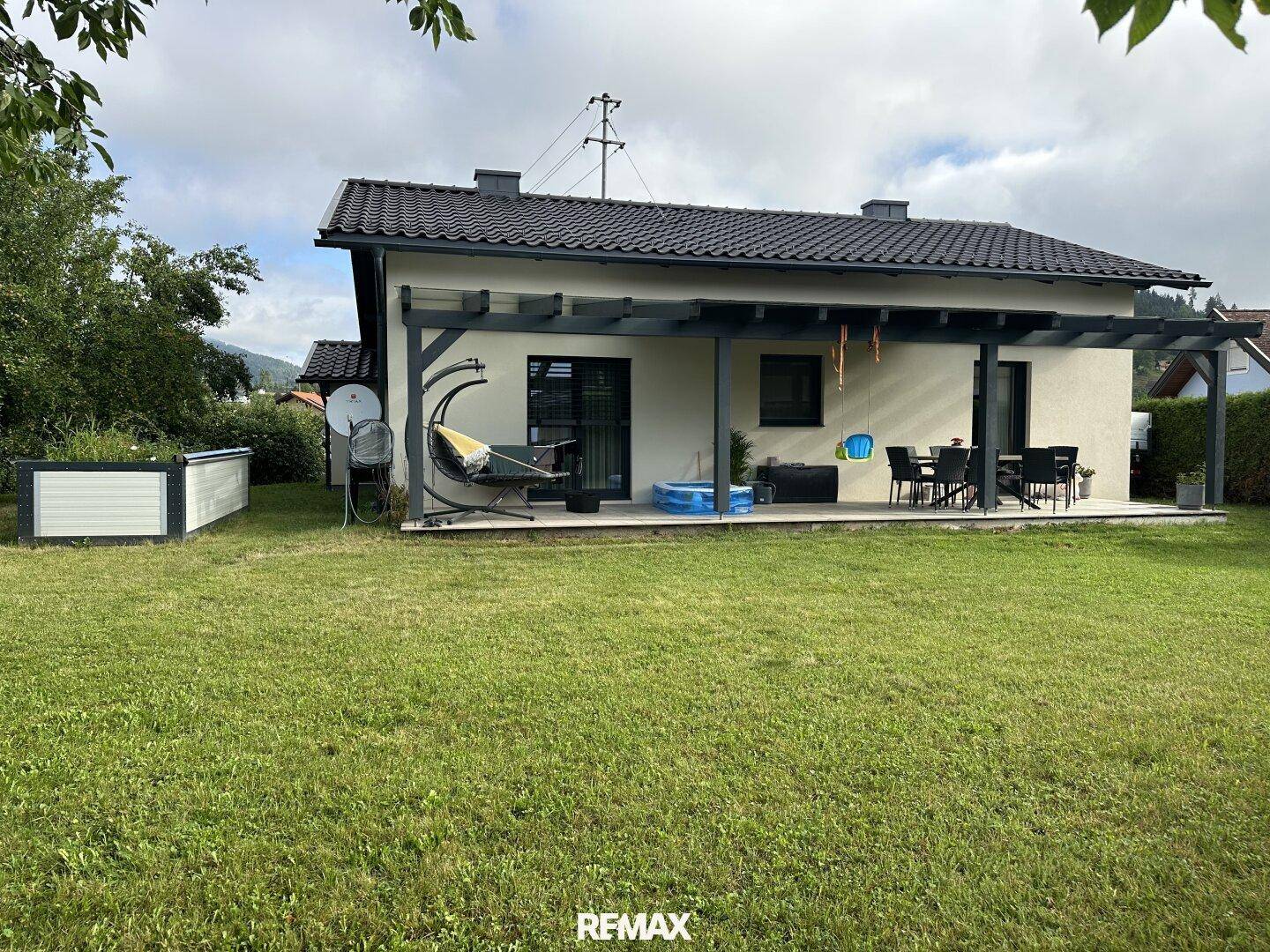 Weitläufiger Gartenbereich mit Rasenfläche und überdachter Terrasse, ideal für Entspannung im Freien.