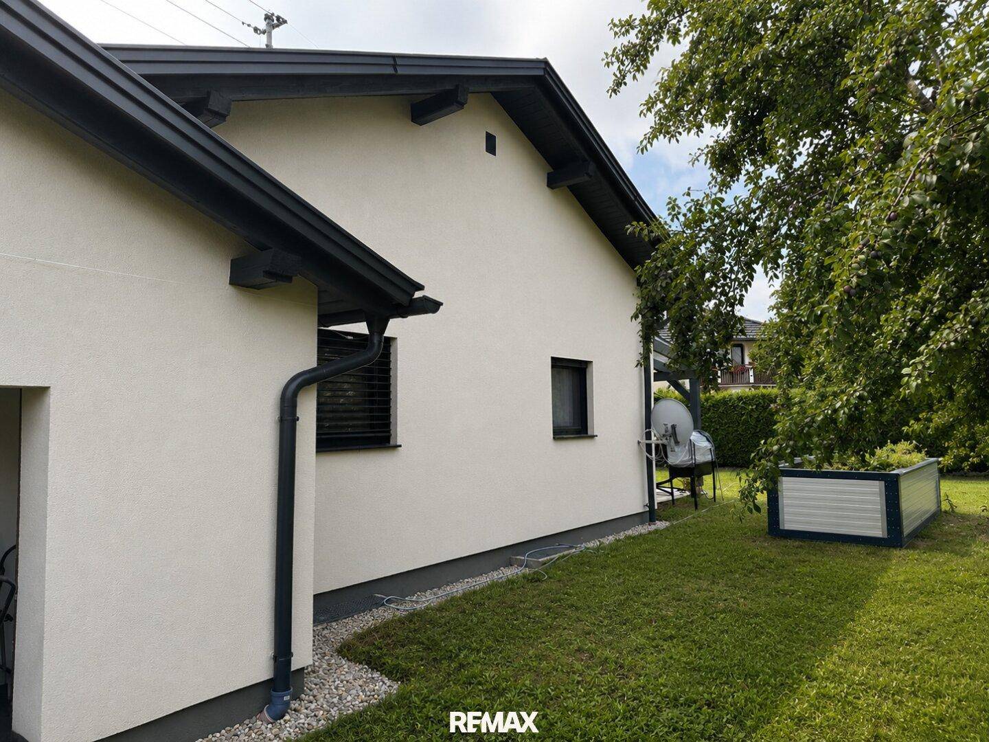 Seitenansicht des Hauses mit Gartenbereich, Hochbeet und angrenzender überdachter Terrasse.