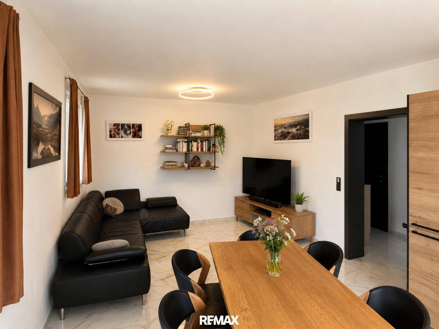 Gemütlicher Wohn- und Essbereich mit modernem Sofa, Fernseher und hellem Fliesenboden.