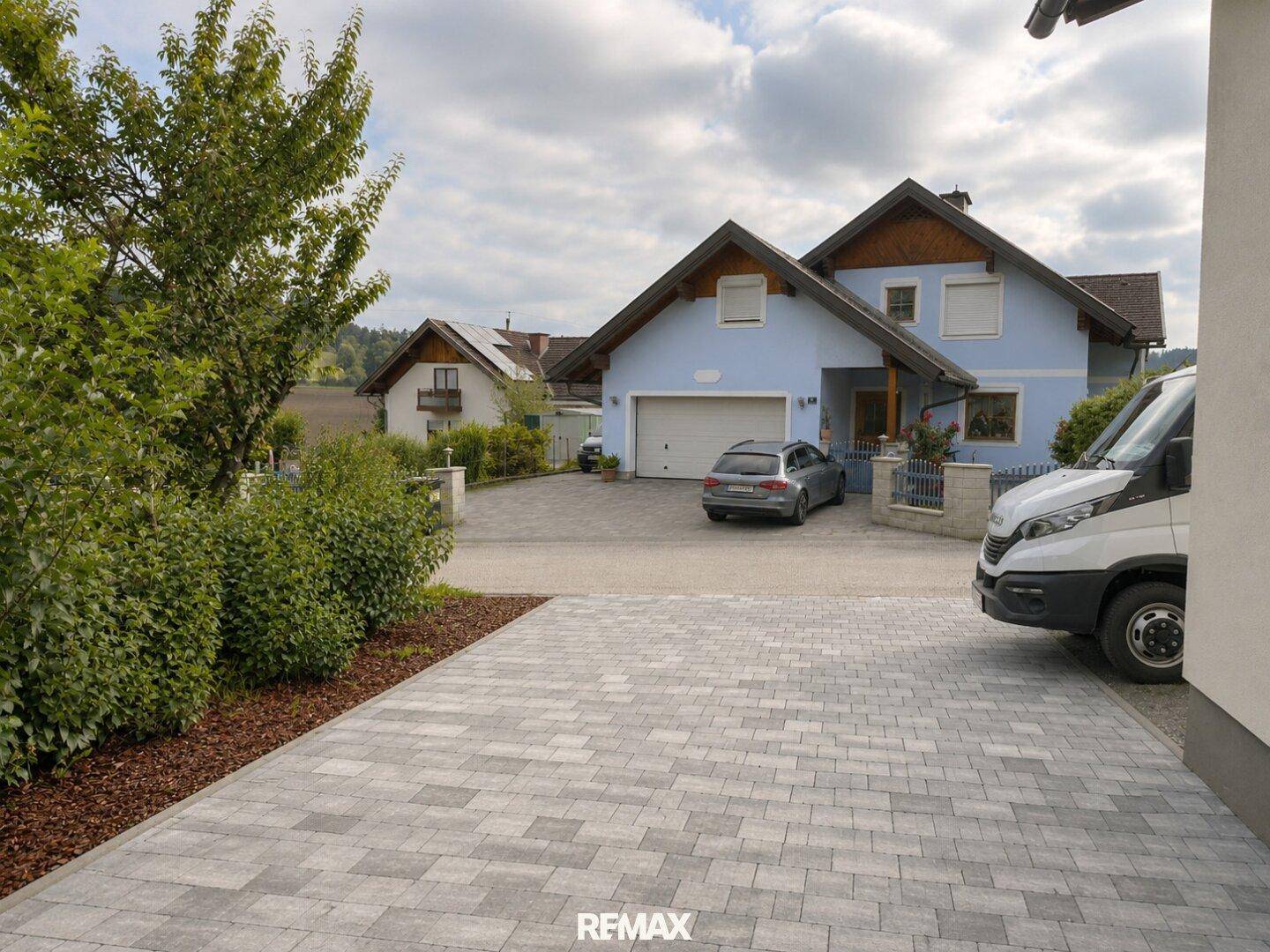 Gepflasterte Zufahrt zum Haus mit angrenzendem Vorgarten und Blick auf die Nachbarschaft.