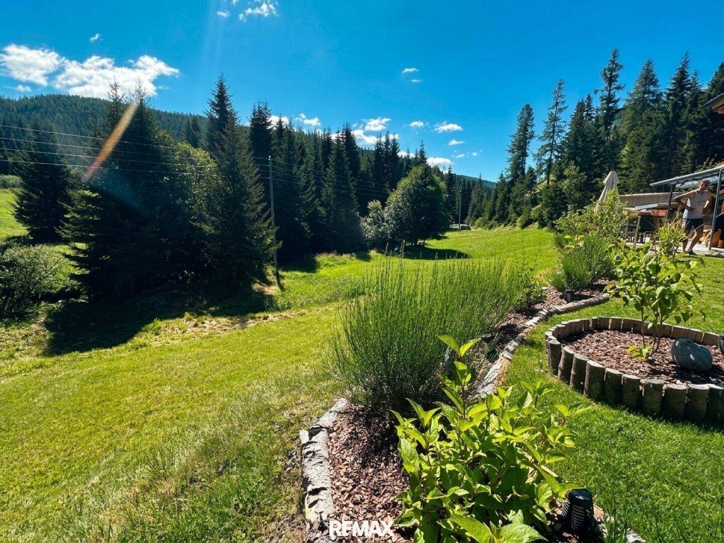 Gartenweg mit Sträuchern und weitem Blick auf den Wald und die umliegenden Berge.