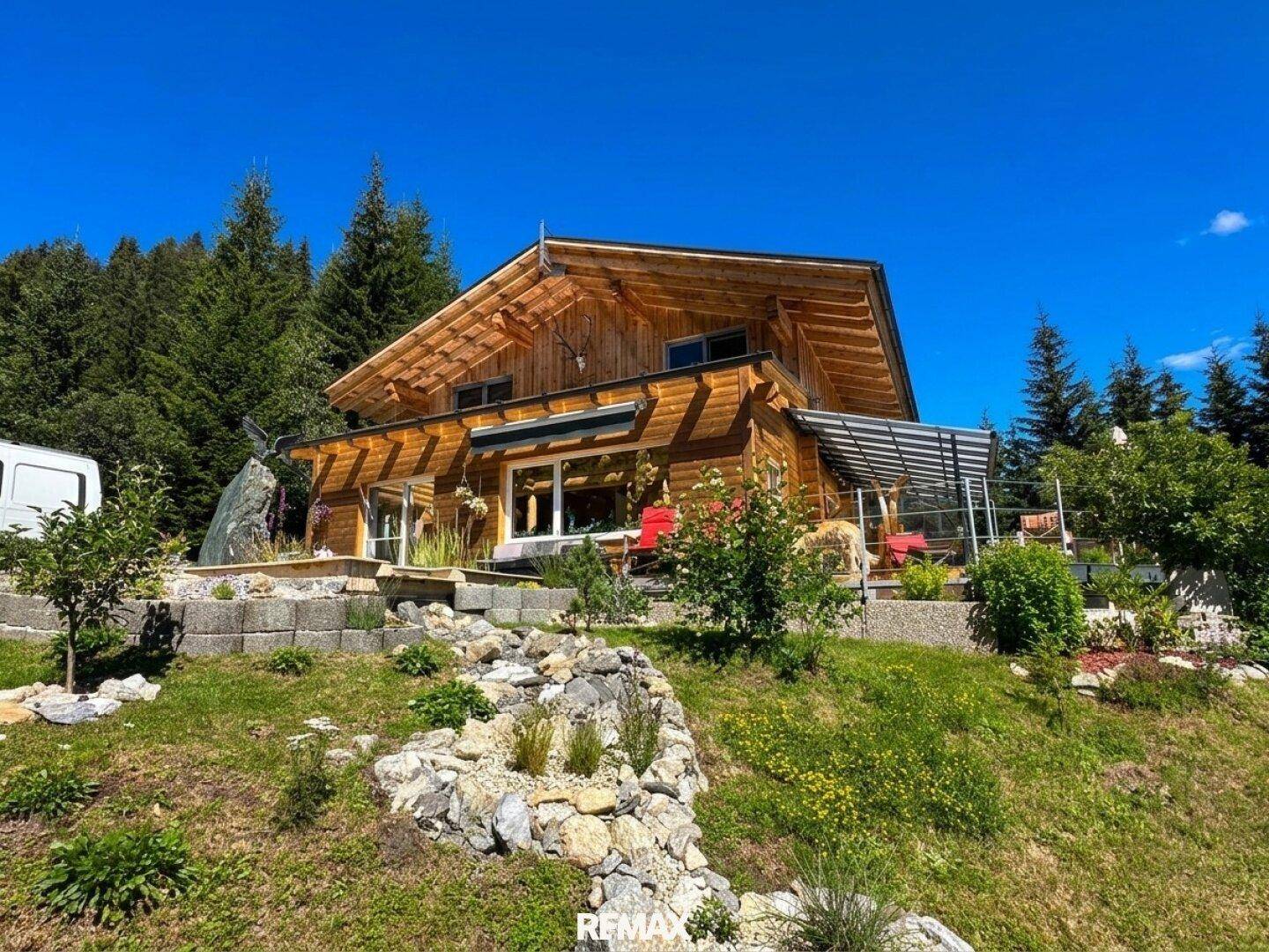 Charmantes Holzchalet mit Satteldach, umgeben von einem gepflegten Garten und Wald.