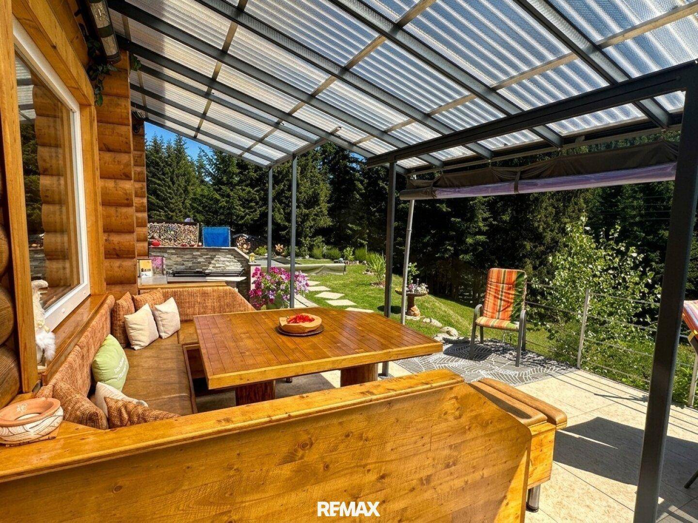 Gemütlicher überdachter Essbereich auf der Terrasse mit rustikalem Holztisch und Bänken.