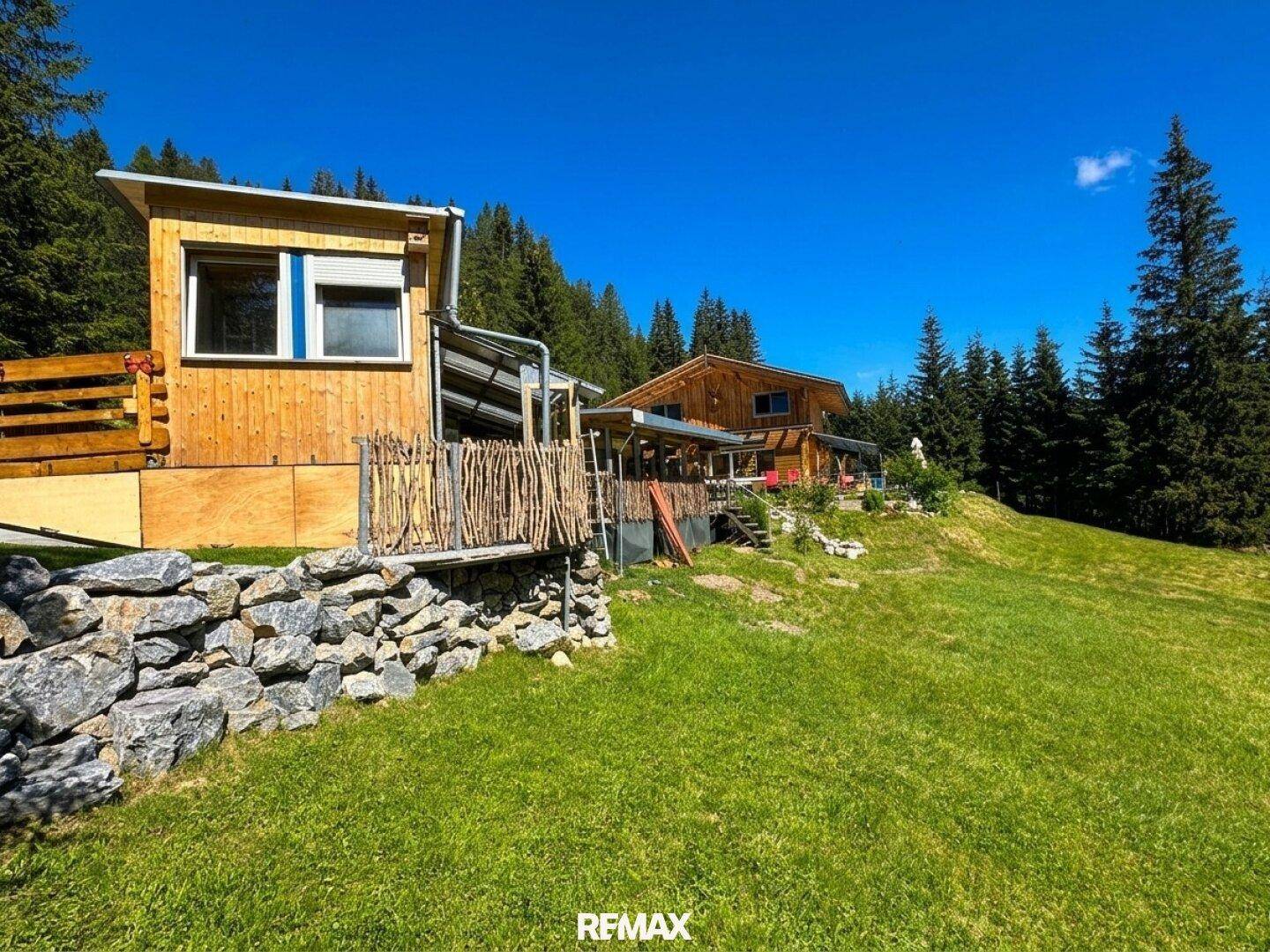 Nebengebäude mit Holzfassade und umgebendem Garten in sonniger alpiner Landschaft.