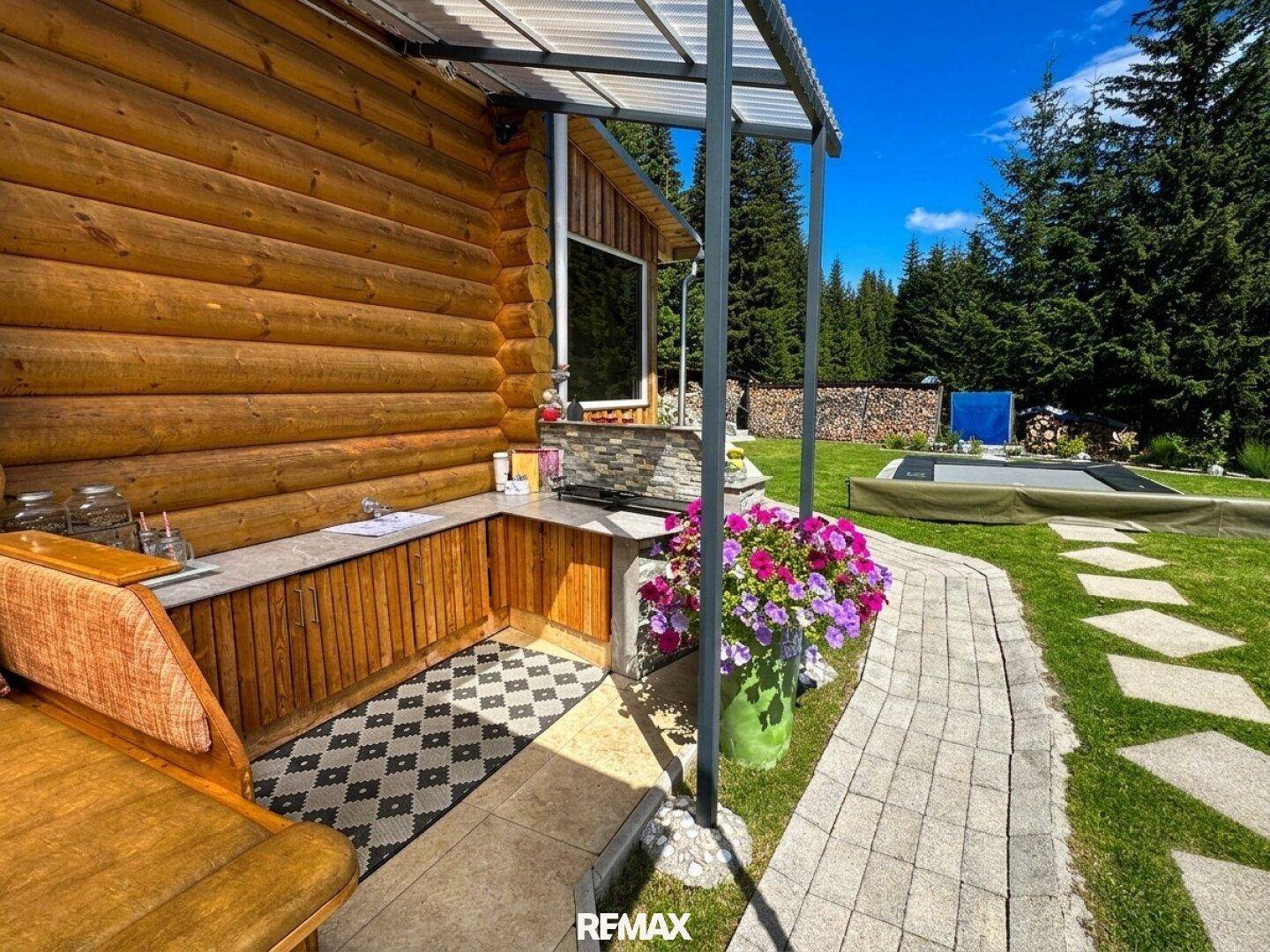 Außenküche mit Grillbereich und gemustertem Teppich, angrenzend an einen gepflasterten Gartenweg.