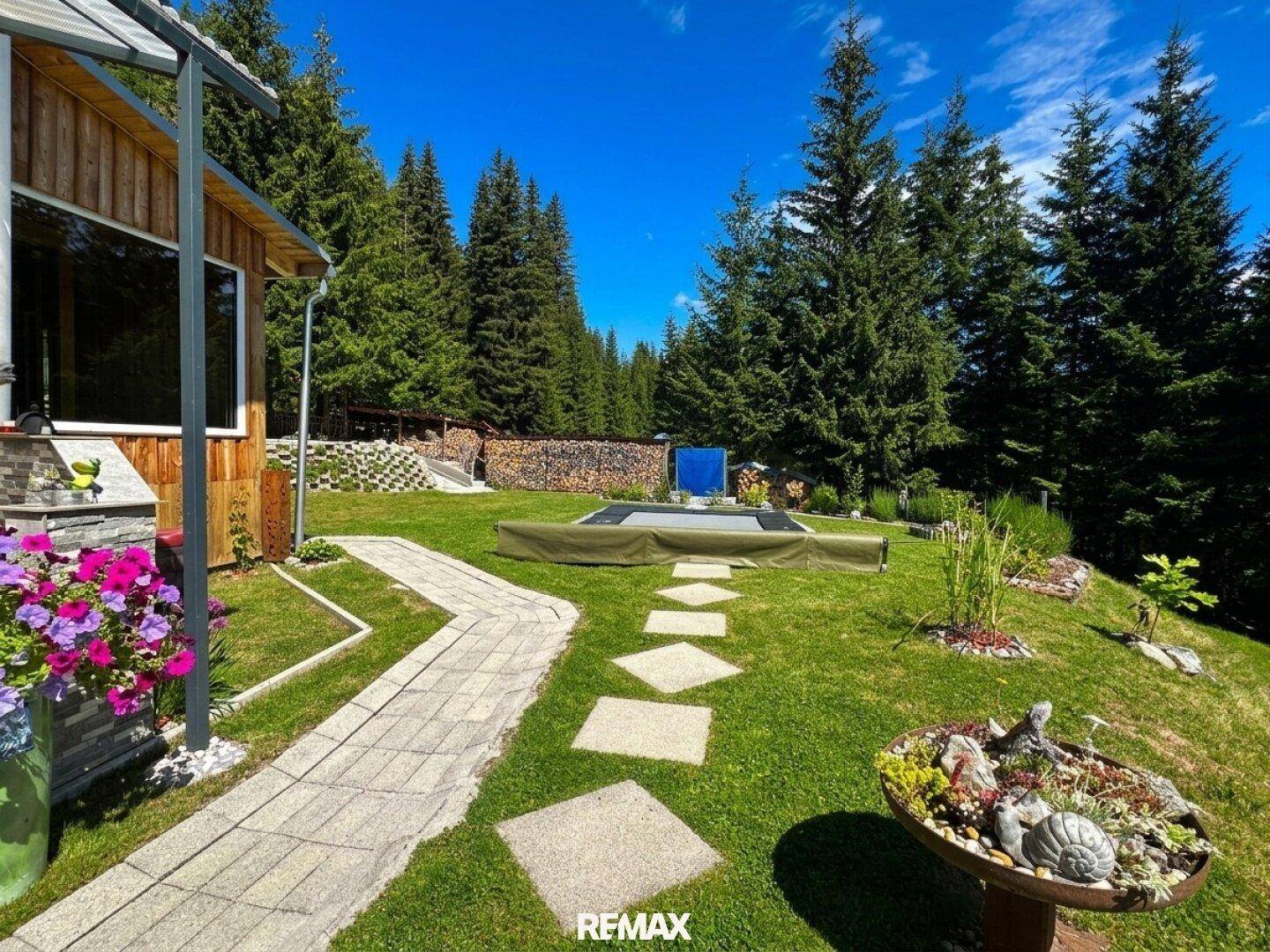 Geschwungener Gartenweg durch eine Rasenfläche mit dekorativen Elementen und Trampolin.