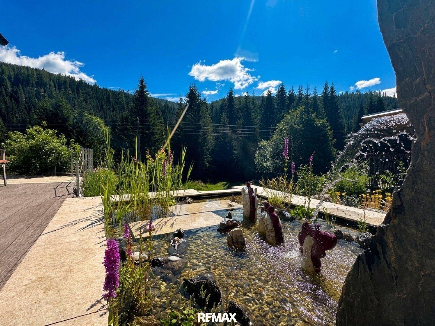 Detailaufnahme eines dekorativen Wasserfalls und Teichs im naturnahen Gartenbereich des Anwesens.