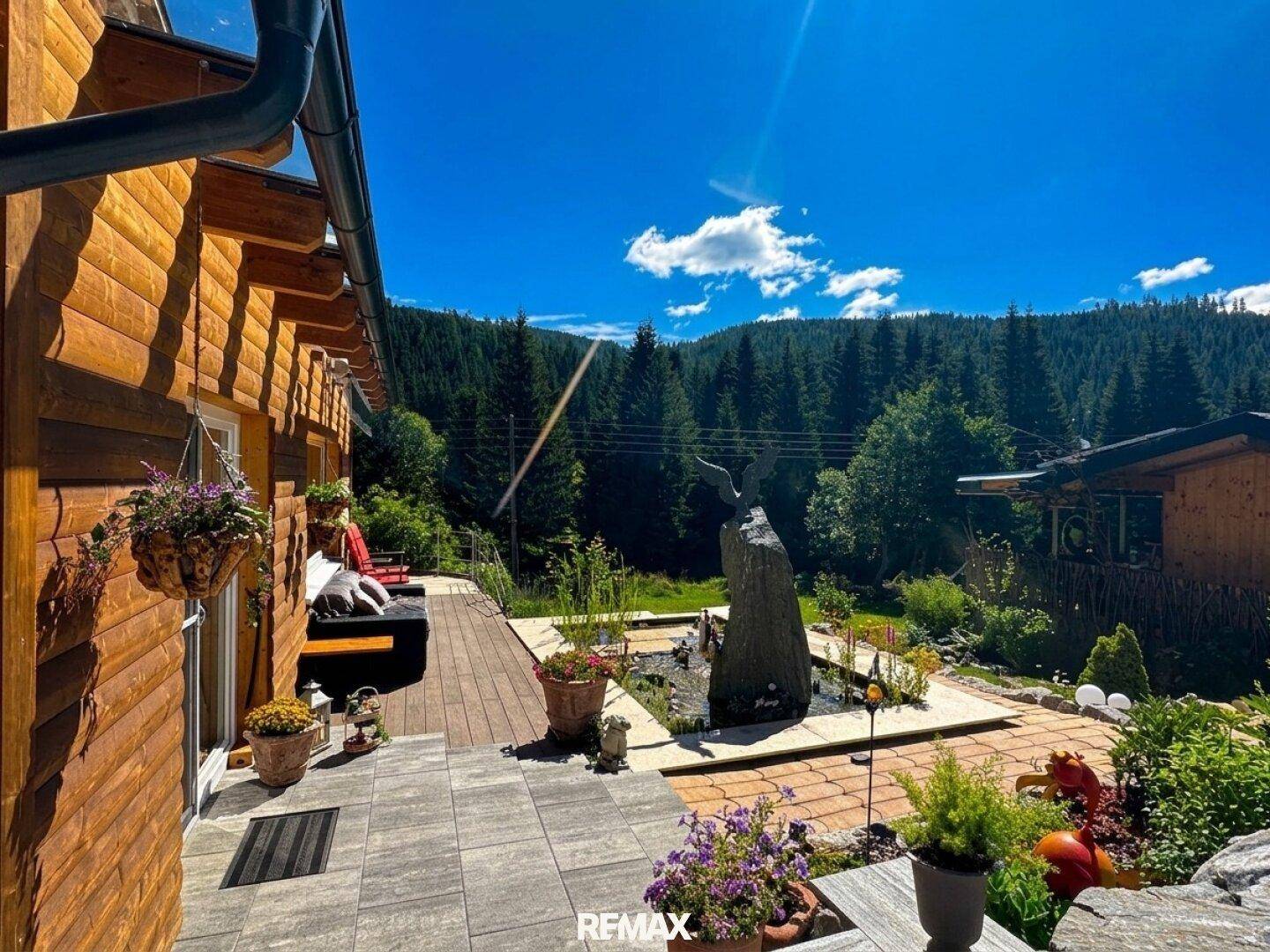 Seitliche Terrasse mit Pflastersteinen, Topfpflanzen und weitem Blick auf den Wald.