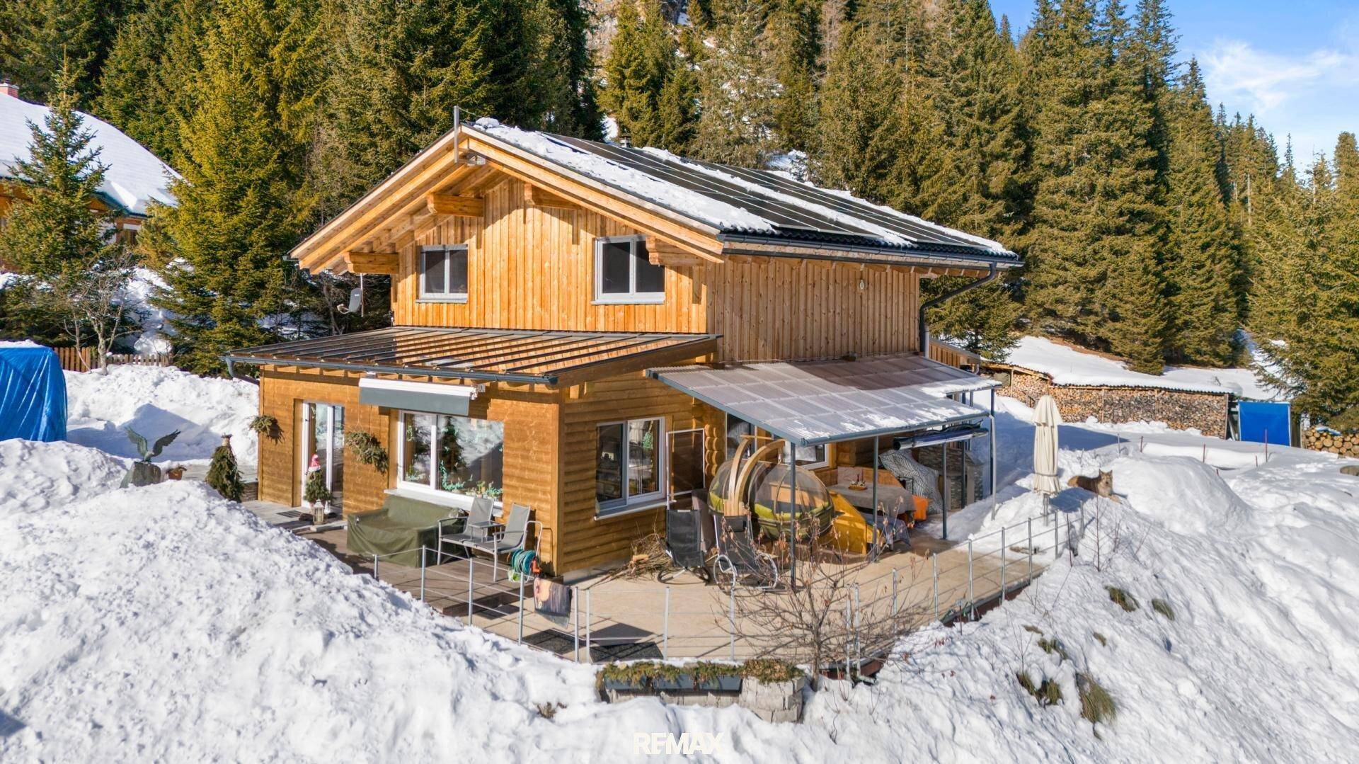 Gemütliches Holzchalet mit möblierter Terrasse und Blick auf die verschneite Berglandschaft.