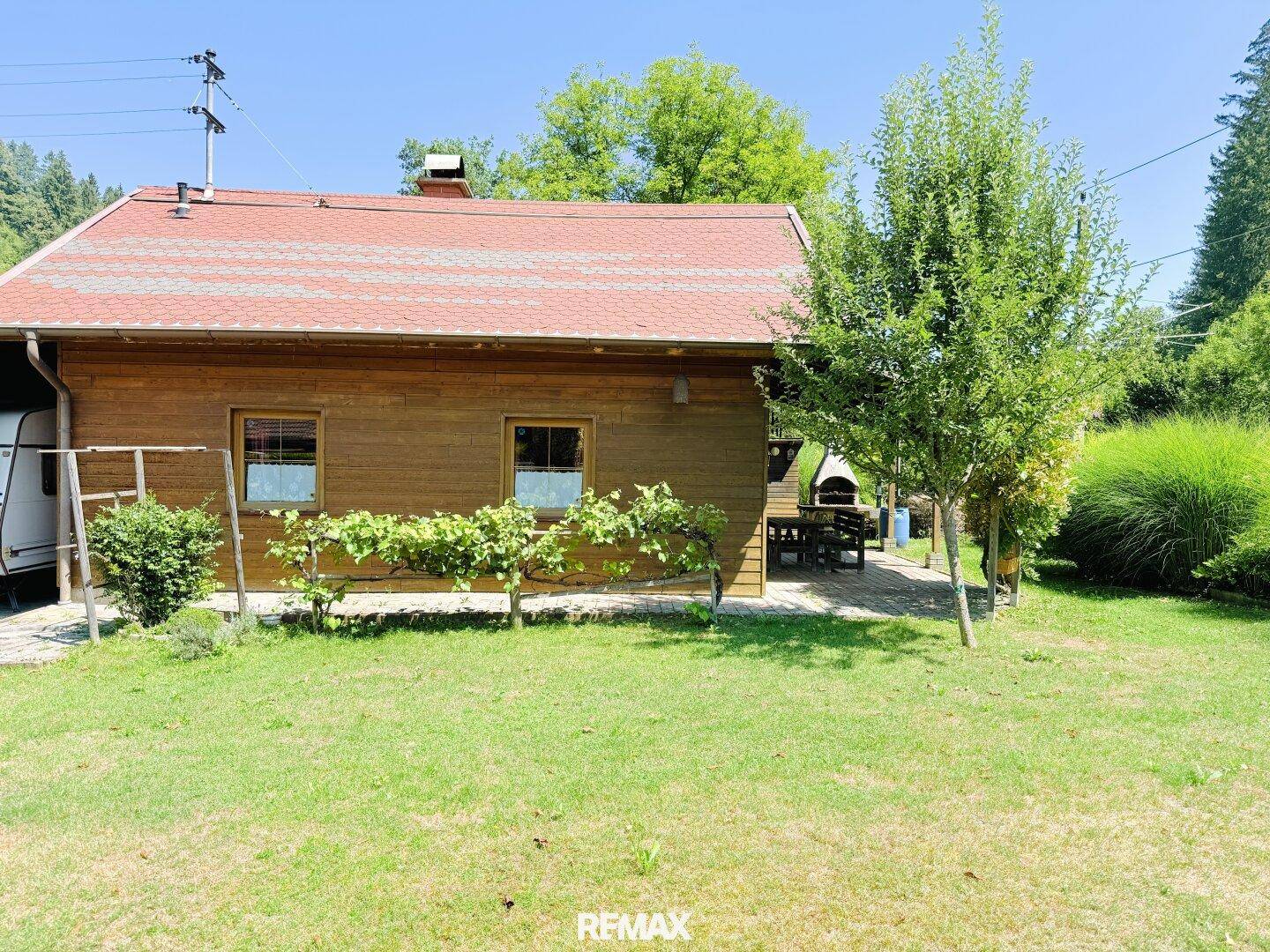 Charmantes Holzhaus mit Garten und einem kleinen Baum im Vordergrund an einem sonnigen Tag.