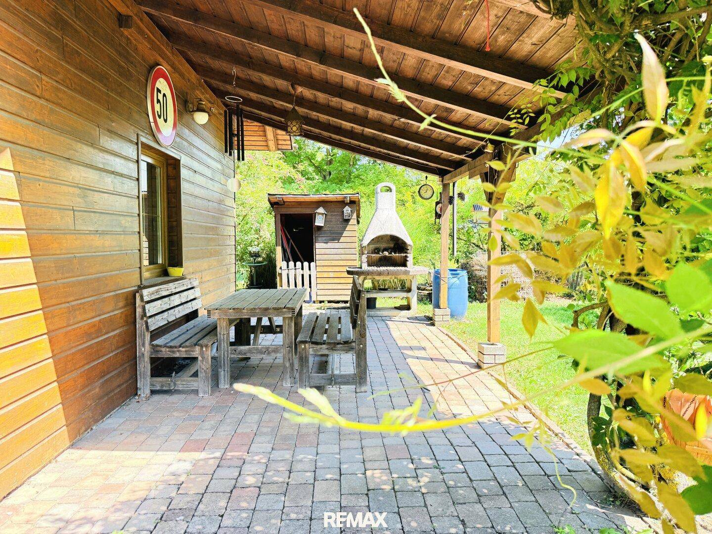 Überdachte Terrasse mit Holztisch und Bänken, ideal für Mahlzeiten im Freien und Grillabende.