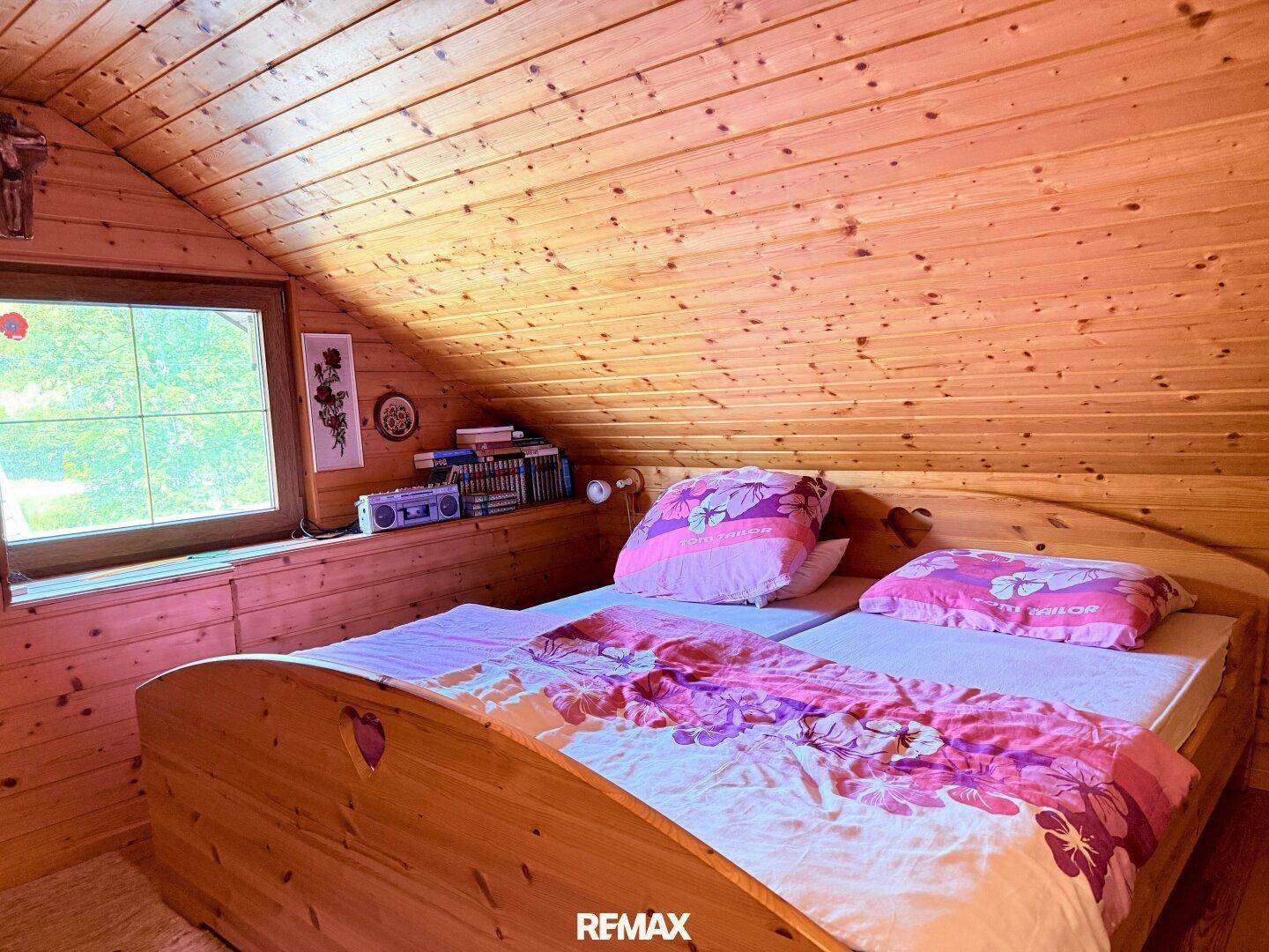 Schlafzimmer mit Holzwänden und -decke, Doppelbett und Fenster mit Blick ins Grüne.