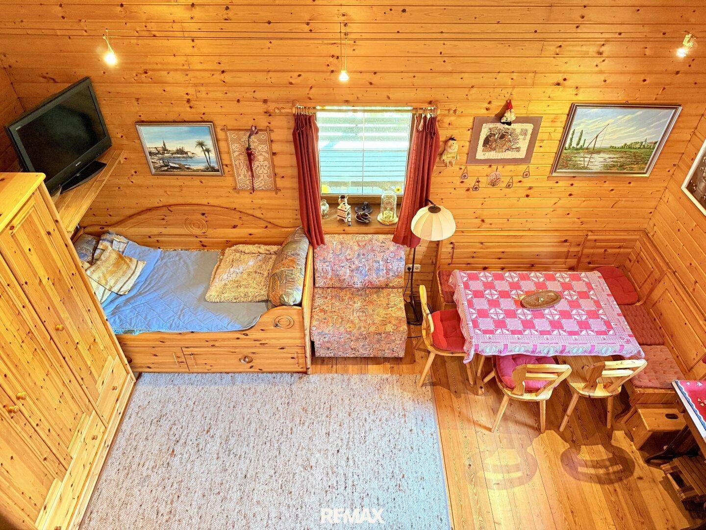 Rustikaler Wohnraum mit Holzwänden und -decken, Schlafgelegenheit und Essbereich unter Dachschrägen.