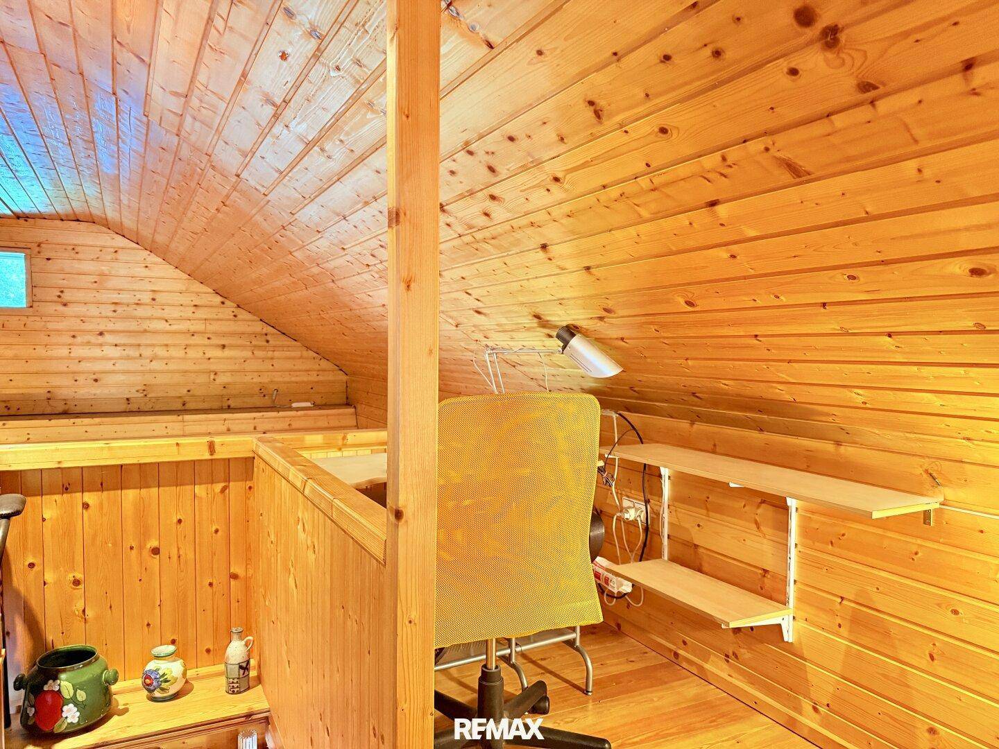 Kleiner Arbeitsbereich unter der Dachschräge mit Holzwänden und Schreibtisch, ideal für konzentriertes Arbeiten.