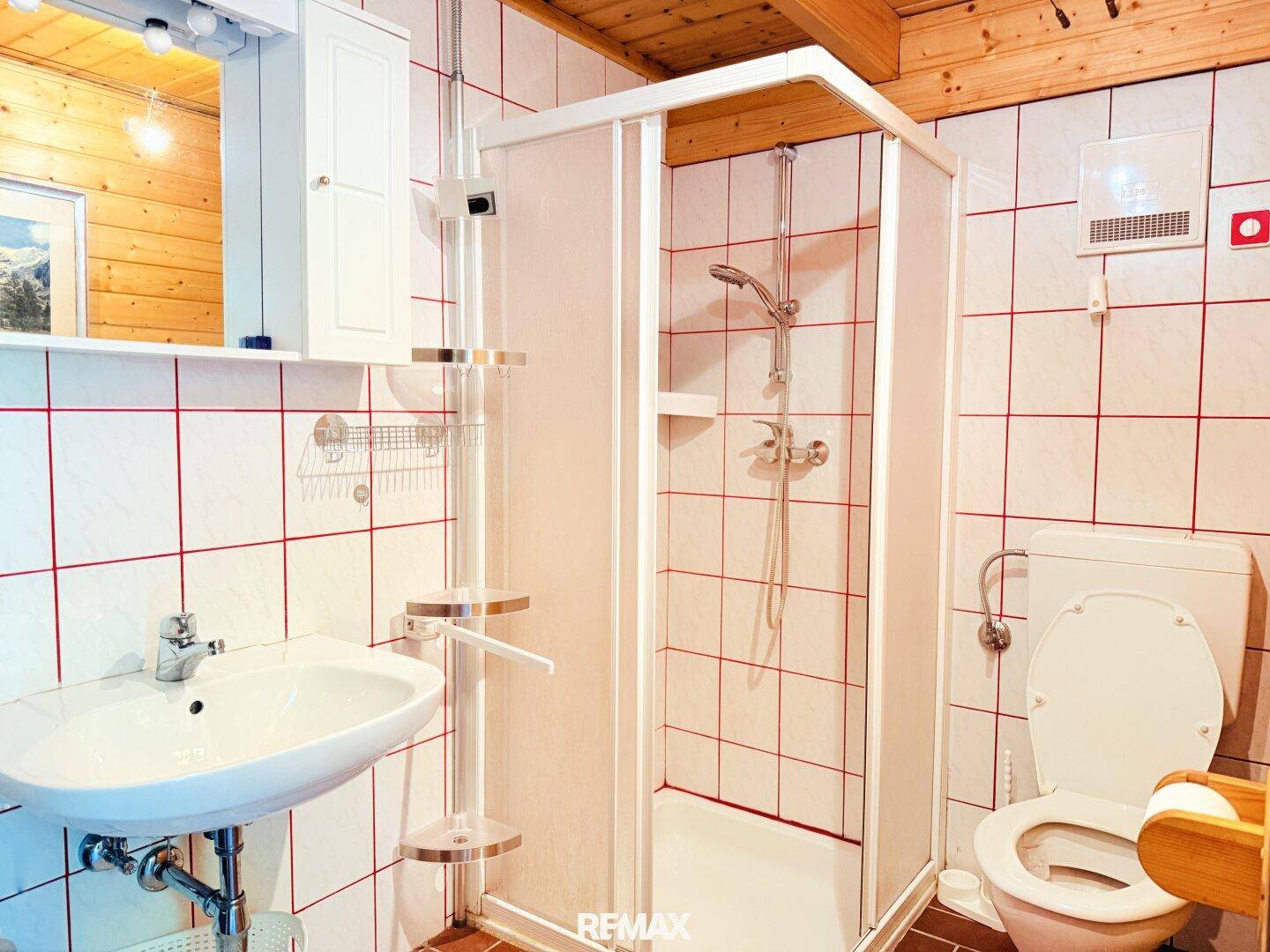 Helles Badezimmer mit Duschkabine, Waschbecken und WC, ausgestattet mit weißen Fliesen und roten Akzenten.