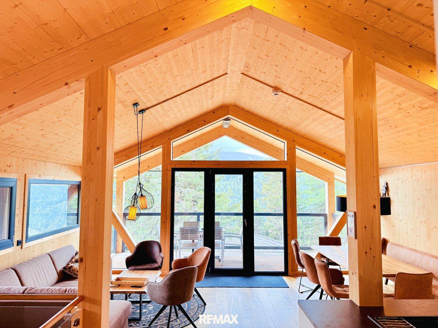 Gemütlicher Wohn-Essbereich mit Holzbalken, hohen Decken und Zugang zum Balkon.