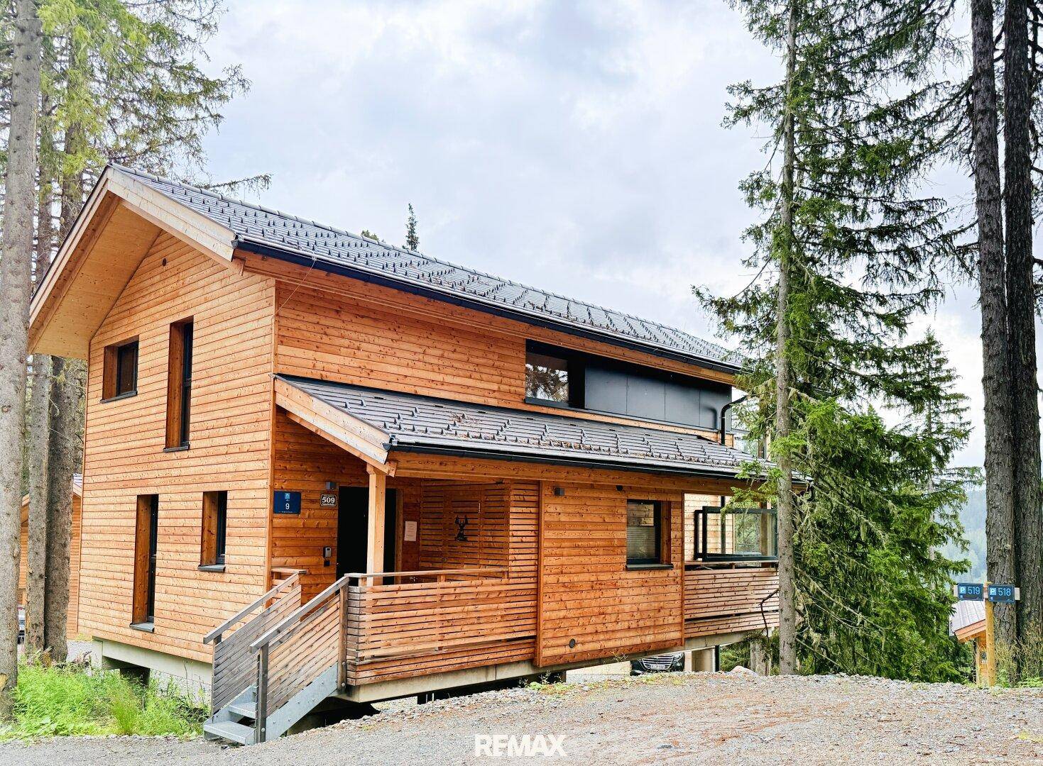 Holzchalet in den Bergen mit traditionellem Satteldach und umgebenden Nadelbäumen.