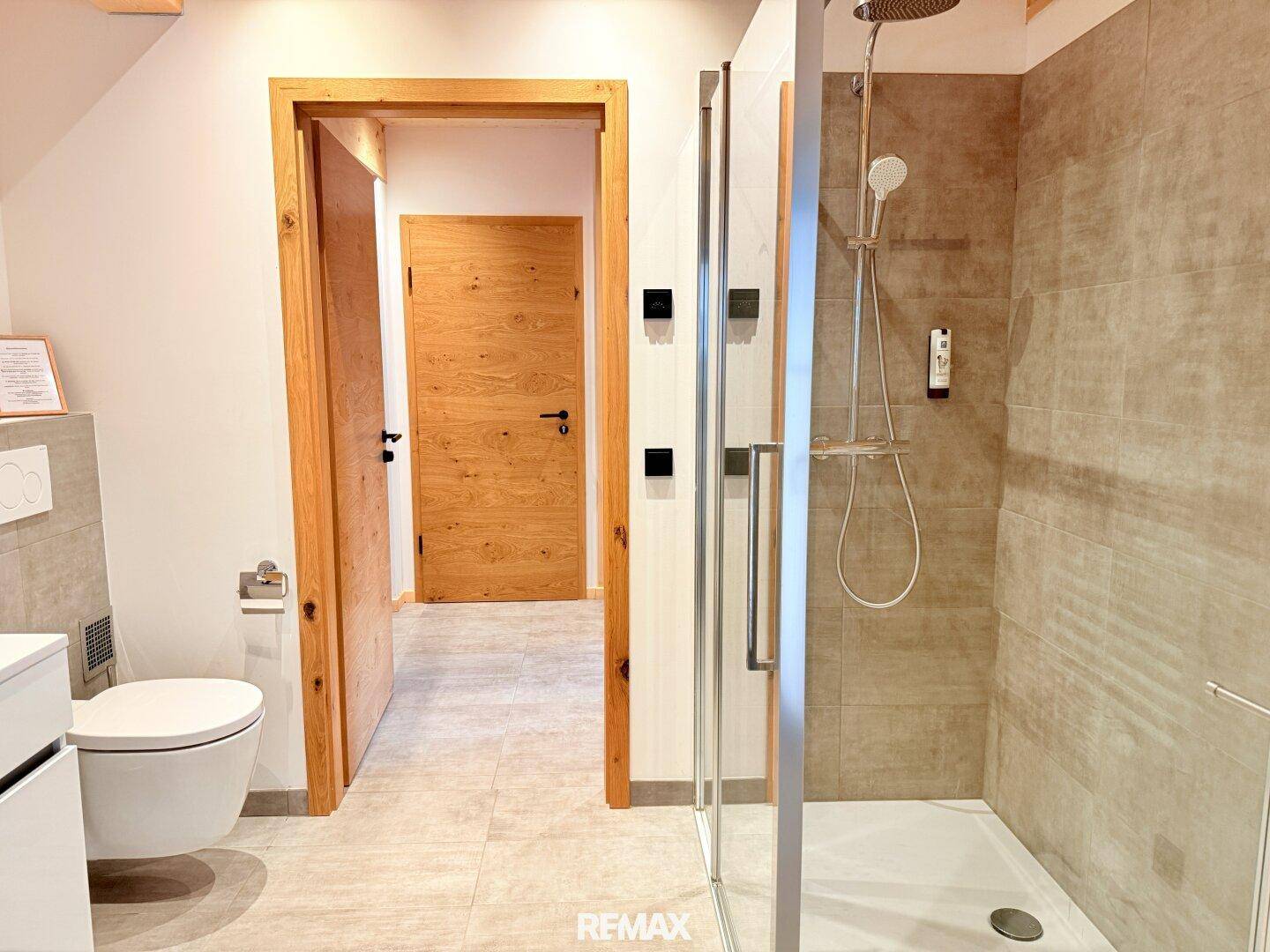 Badezimmer mit ebenerdiger Dusche, Wand-WC und modernen Fliesen in neutralen Farben.