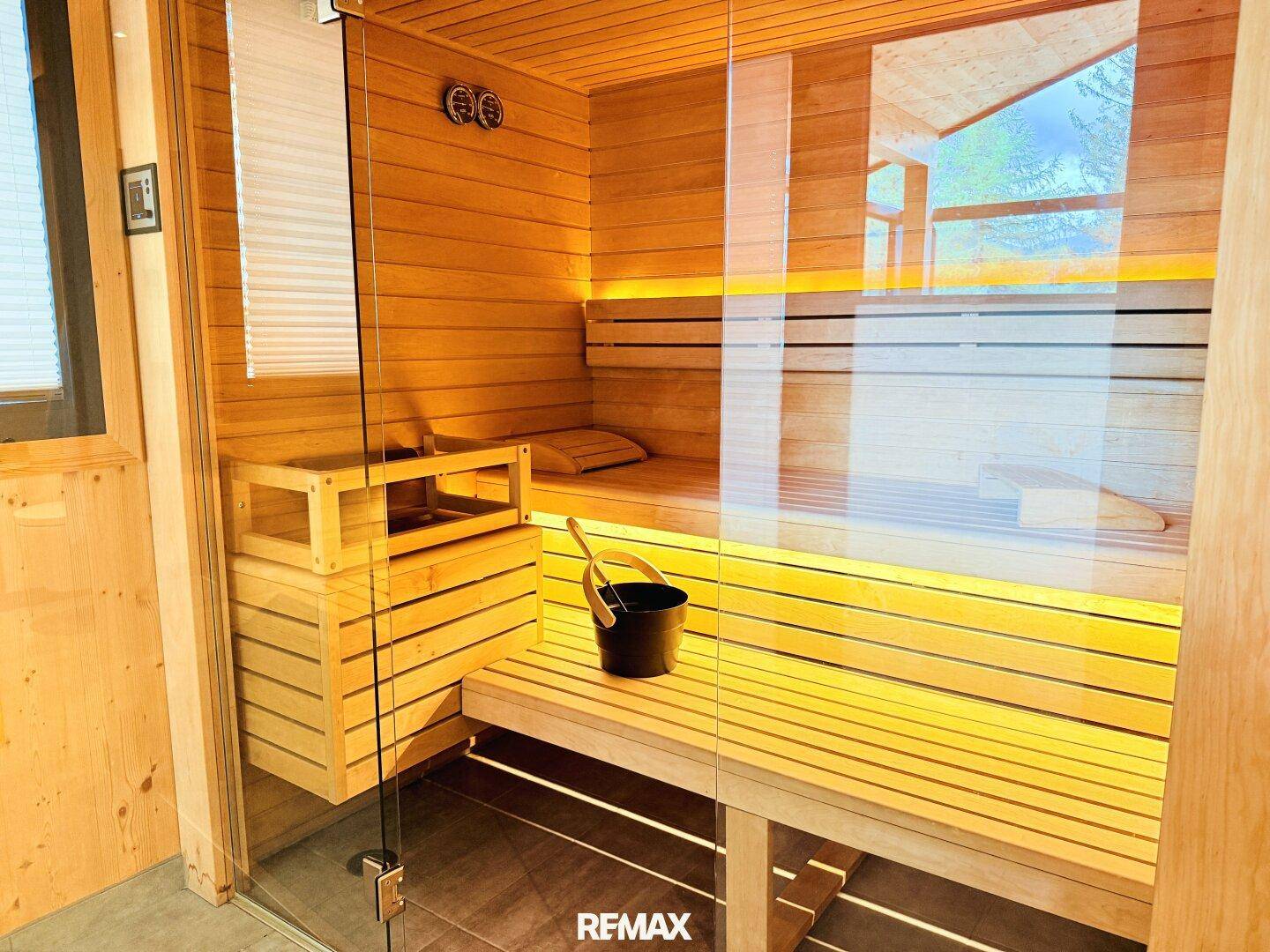 Moderne Holzsauna mit Glasfront, Bänken und stimmungsvoller Beleuchtung.