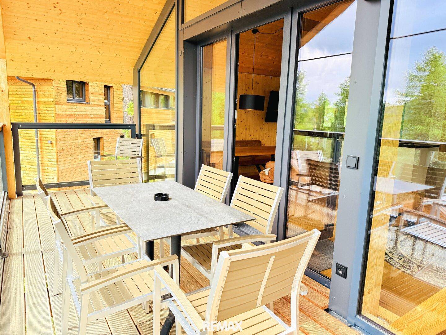 Sonniger Balkon mit Holzboden, Esstisch und Zugang zum Innenbereich durch große Glastüren.