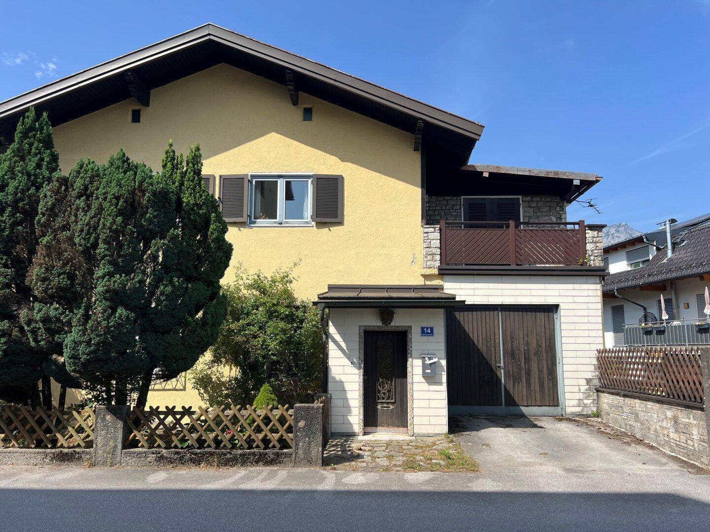 Gelbes Haus mit braunen Fensterläden, Garage und kleinem Balkon unter blauem Himmel.