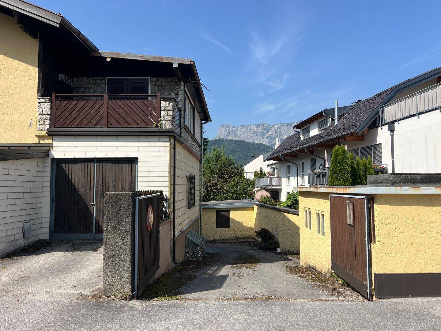 Seitenansicht des Hauses mit Zufahrt und Blick auf die entfernten Berge im Hintergrund.