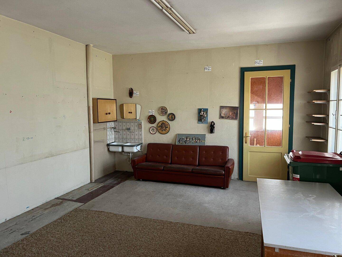 Geräumiger Innenraum mit Sofa, kleinem Waschbecken und einfacher Einrichtung, renovierungsbedürftig.