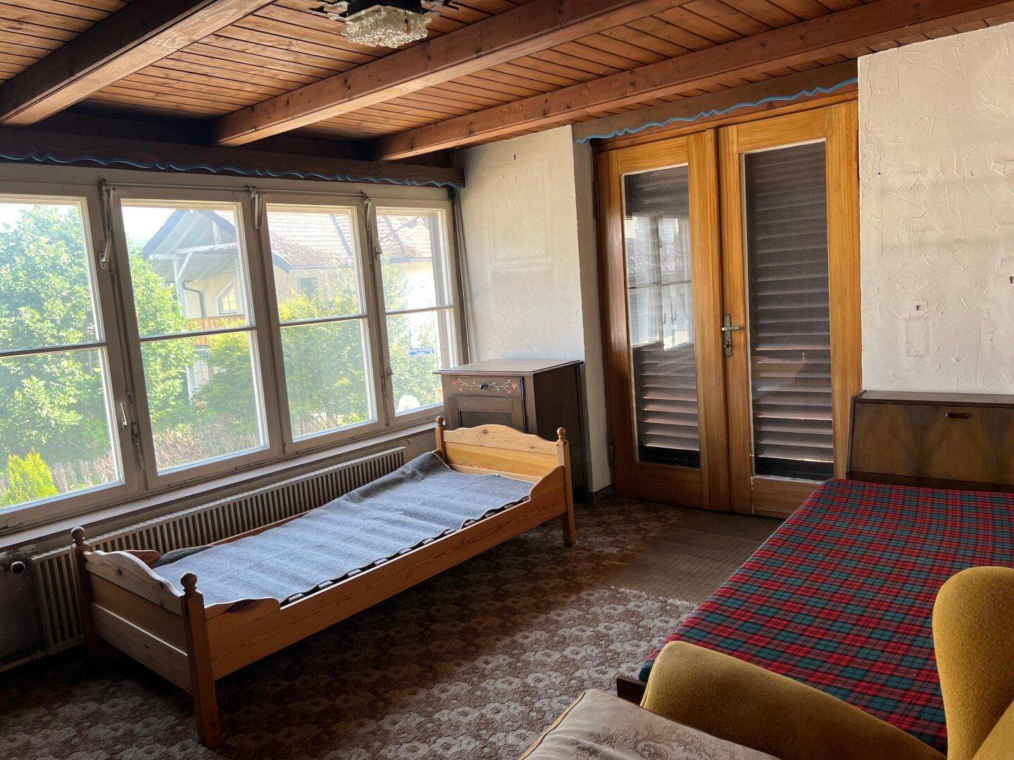 Schlafzimmer mit Holzbalkendecke, zwei Betten und großen Fenstern mit Blick ins Grüne.