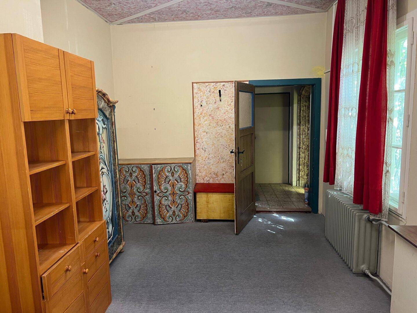 Innenraum mit Holzschrank, dekorativen Elementen und Teppichboden, renovierungsbedürftig und altmodisch.