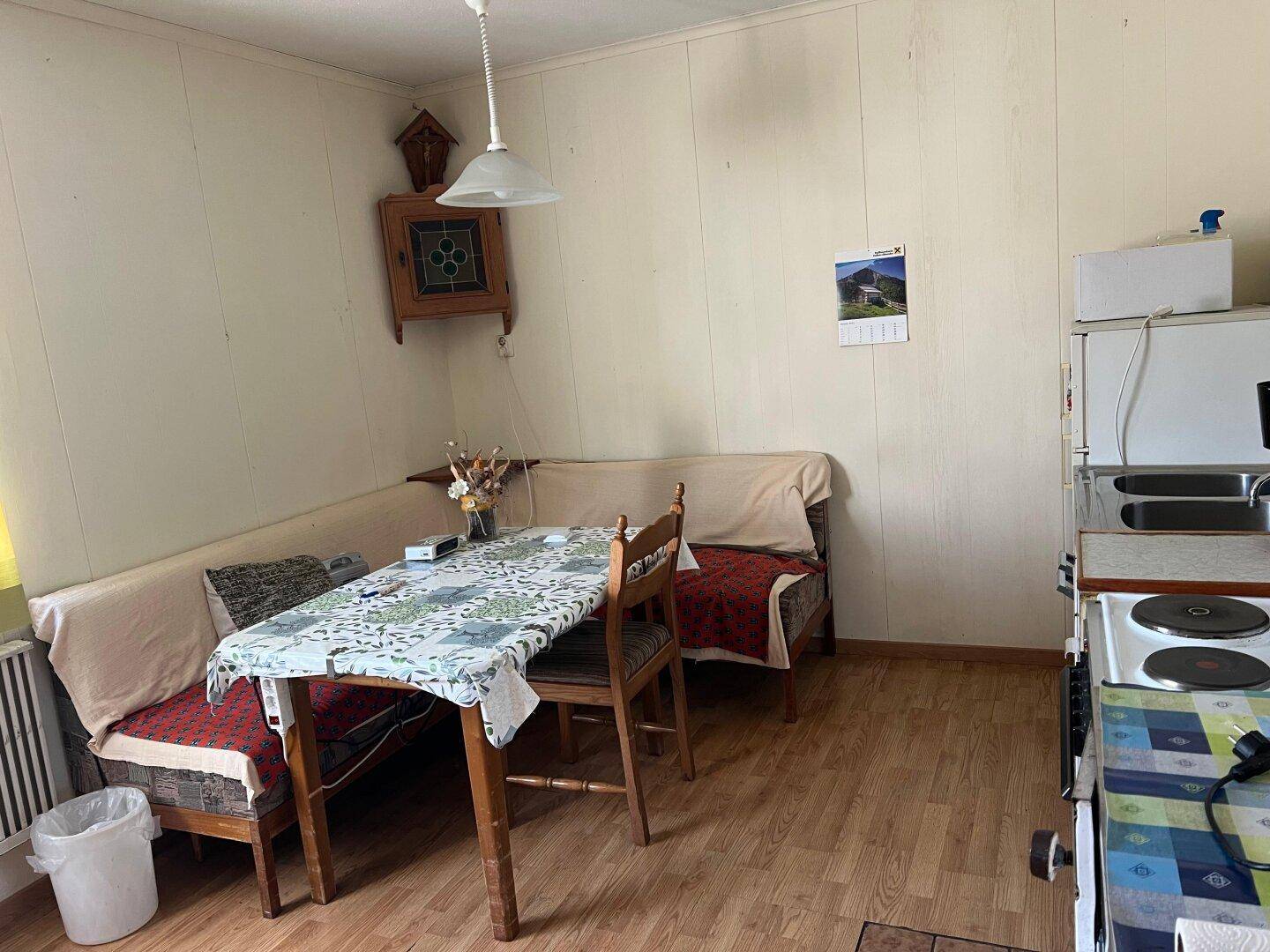 Einfache Küche mit Essecke, Holzvertäfelung und älteren Elektrogeräten, renovierungsbedürftig.