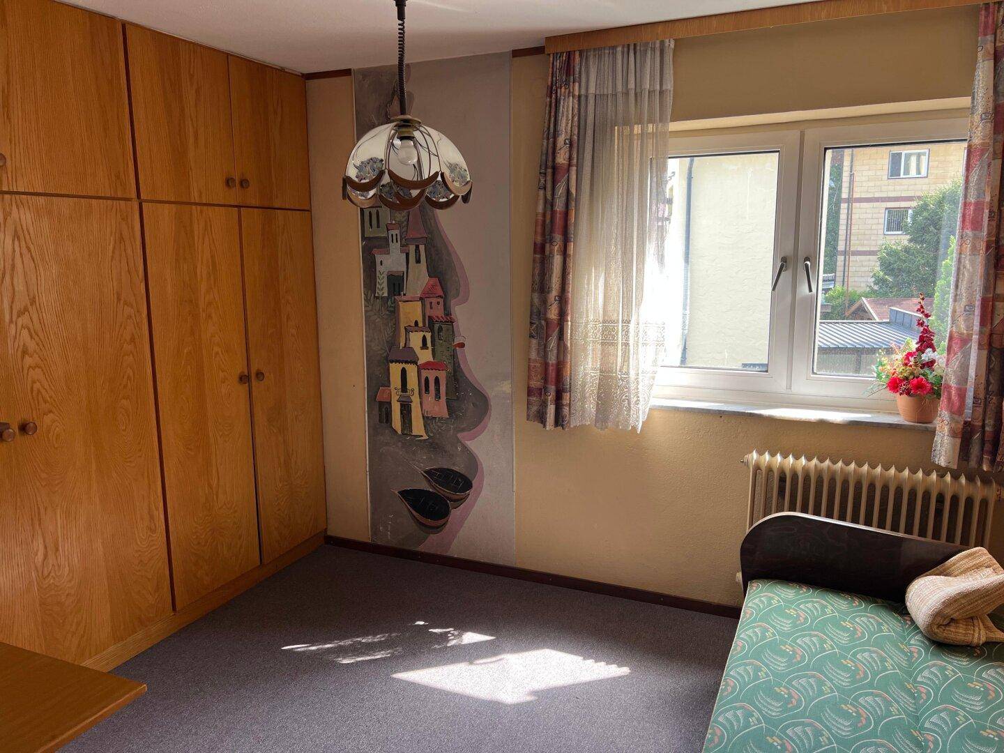Schlafzimmer mit Einbauschränken, Einzelbett und Fenster, renovierungsbedürftig und hell.