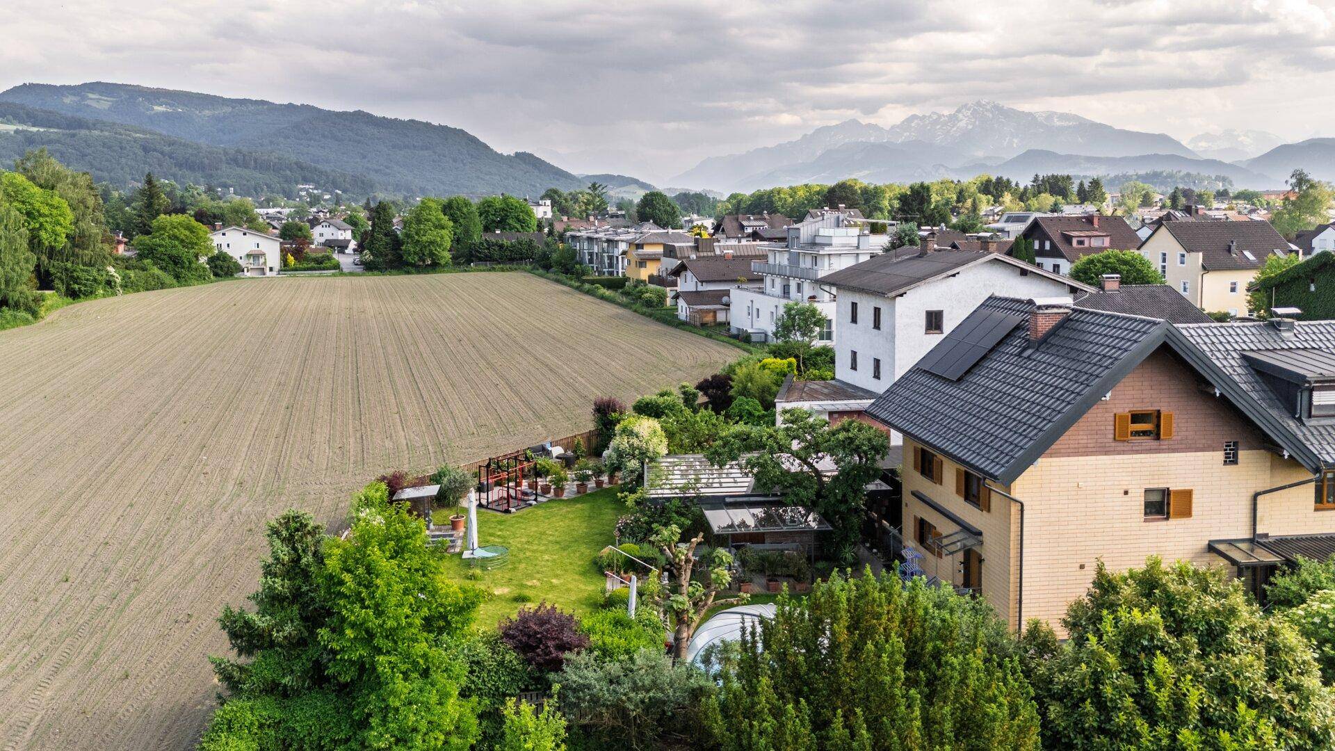 Luftaufnahme einer Wohngegend mit Feldern und Bergen unter bewölktem Himmel.