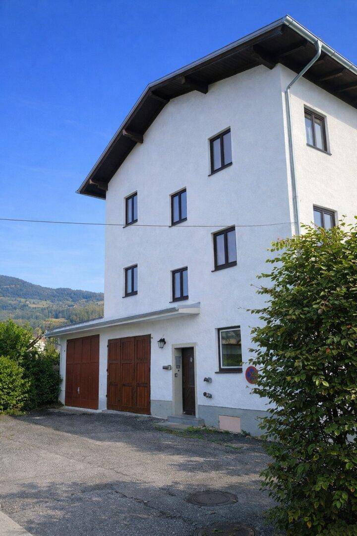 Weißes Mehrfamilienhaus mit braunen Fenstern und Garagentoren unter strahlend blauem Himmel.