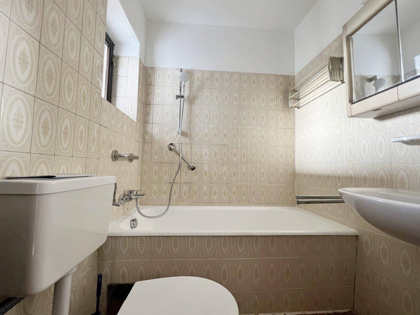 Badezimmer mit Badewanne, WC und beigefarbenen Fliesen, ausgestattet mit Spiegelschrank.