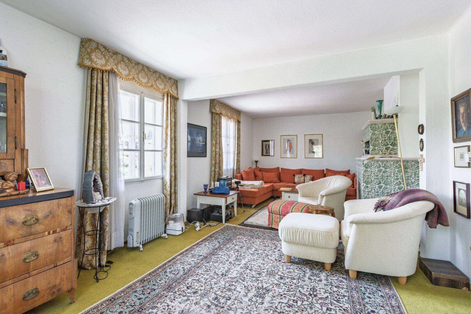 Geräumiges Wohnzimmer mit traditionellem Kachelofen, Teppich und gemütlicher Sitzecke.