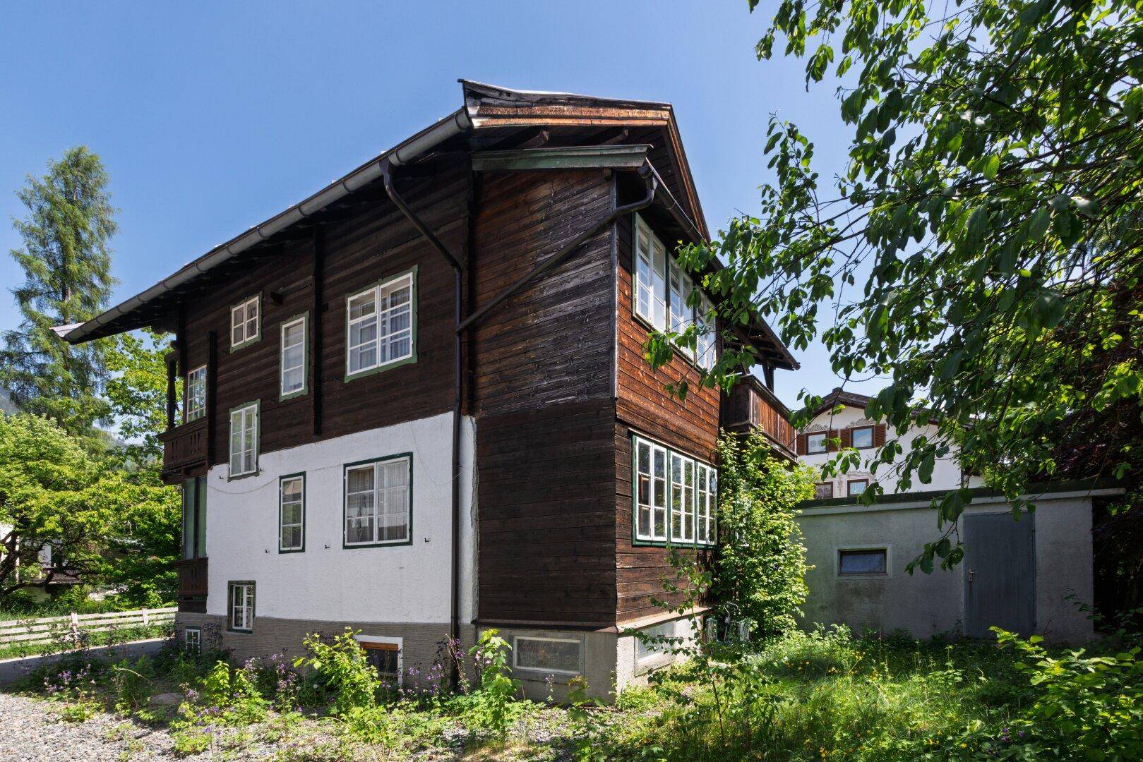Seitenansicht des traditionellen Holzhauses mit weißer Fassade und grüner Umgebung.