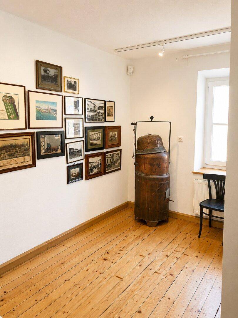 Raum mit Holzdielenboden, einer Wand voller gerahmter Bilder und einem antiken Ofen neben dem Fenster.