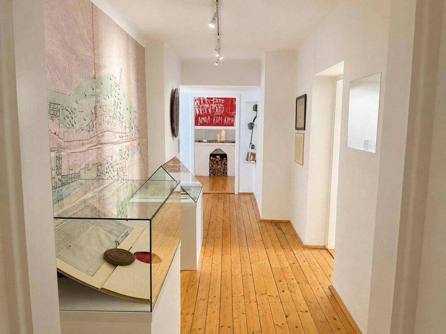 Heller Flur mit Holzdielenboden, Ausstellungsstücken in Vitrinen und einer historischen Karte an der Wand.