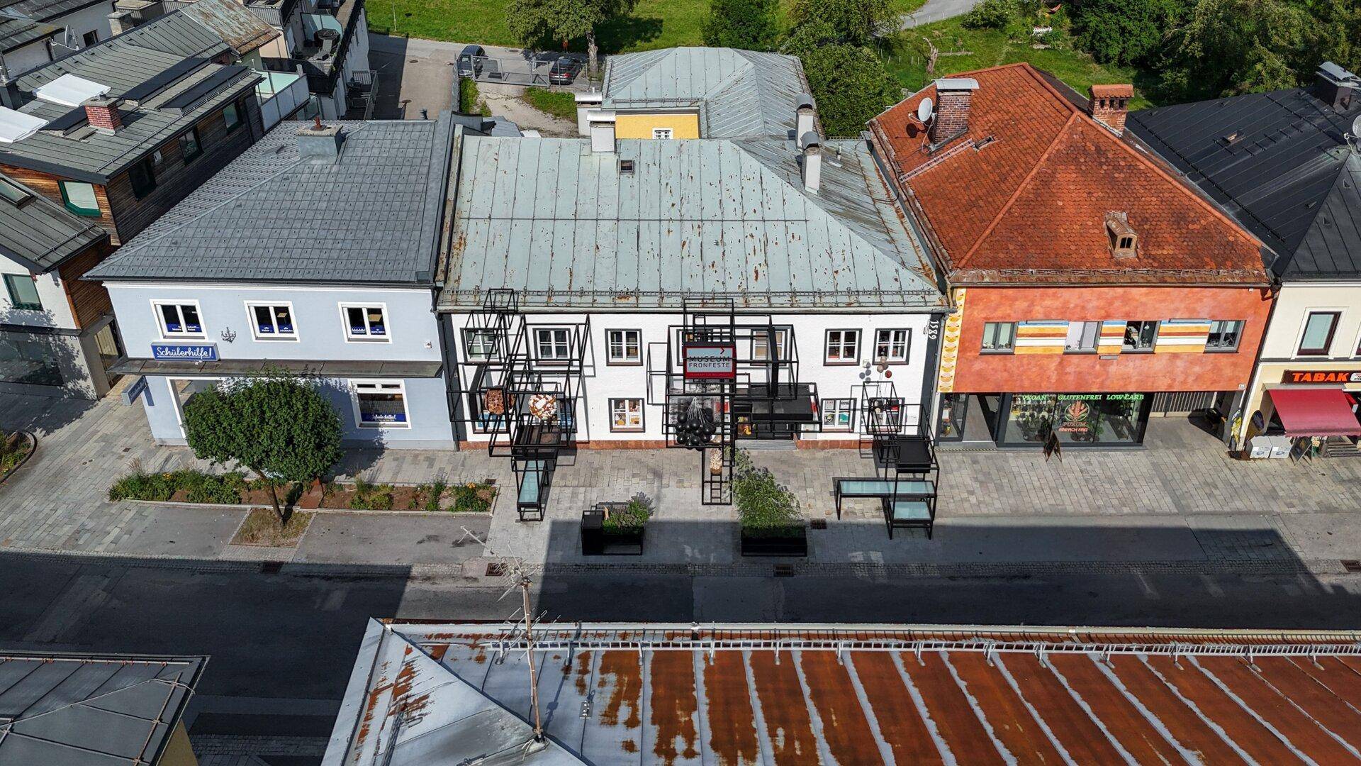 Luftaufnahme einer Straße mit mehreren Gebäuden, darunter das weiße Haus mit der schwarzen Metallkonstruktion.