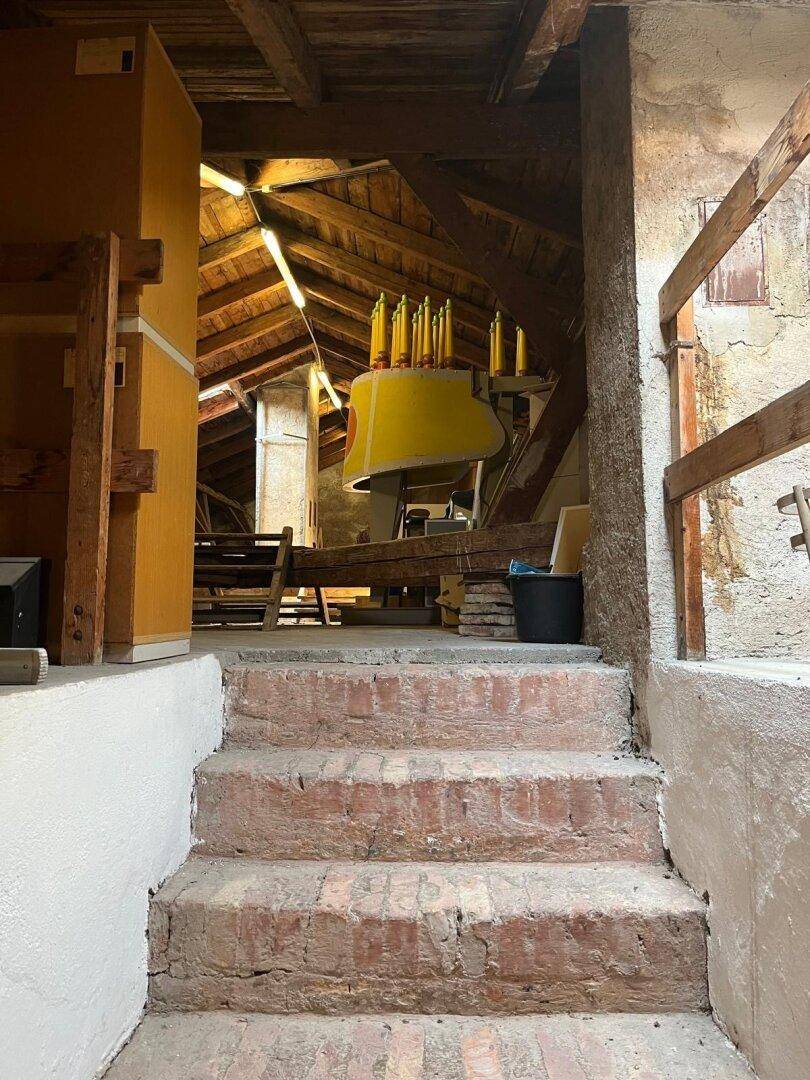 Rustikale Ziegelsteintreppe führt hinauf zu einem Dachboden mit sichtbaren Holzbalken und Lagerflächen.