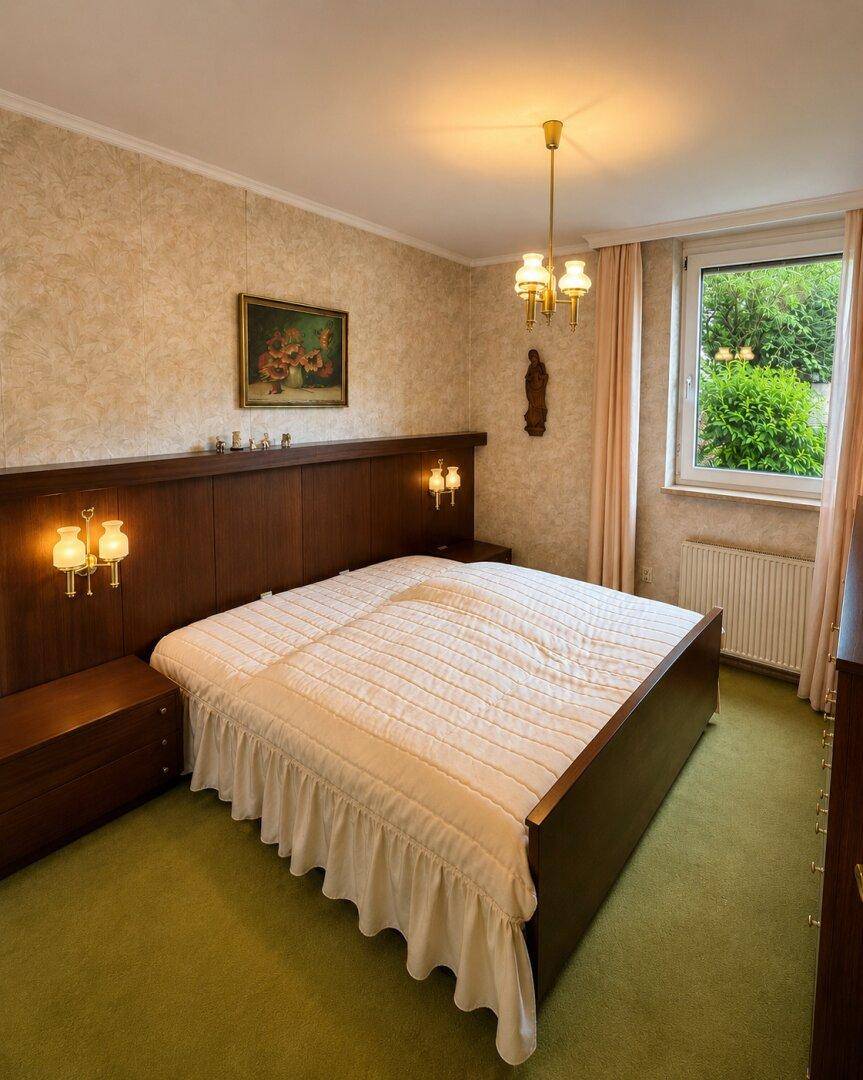 Traditionelles Schlafzimmer mit Teppichboden, Holzbett und Blick ins Grüne.