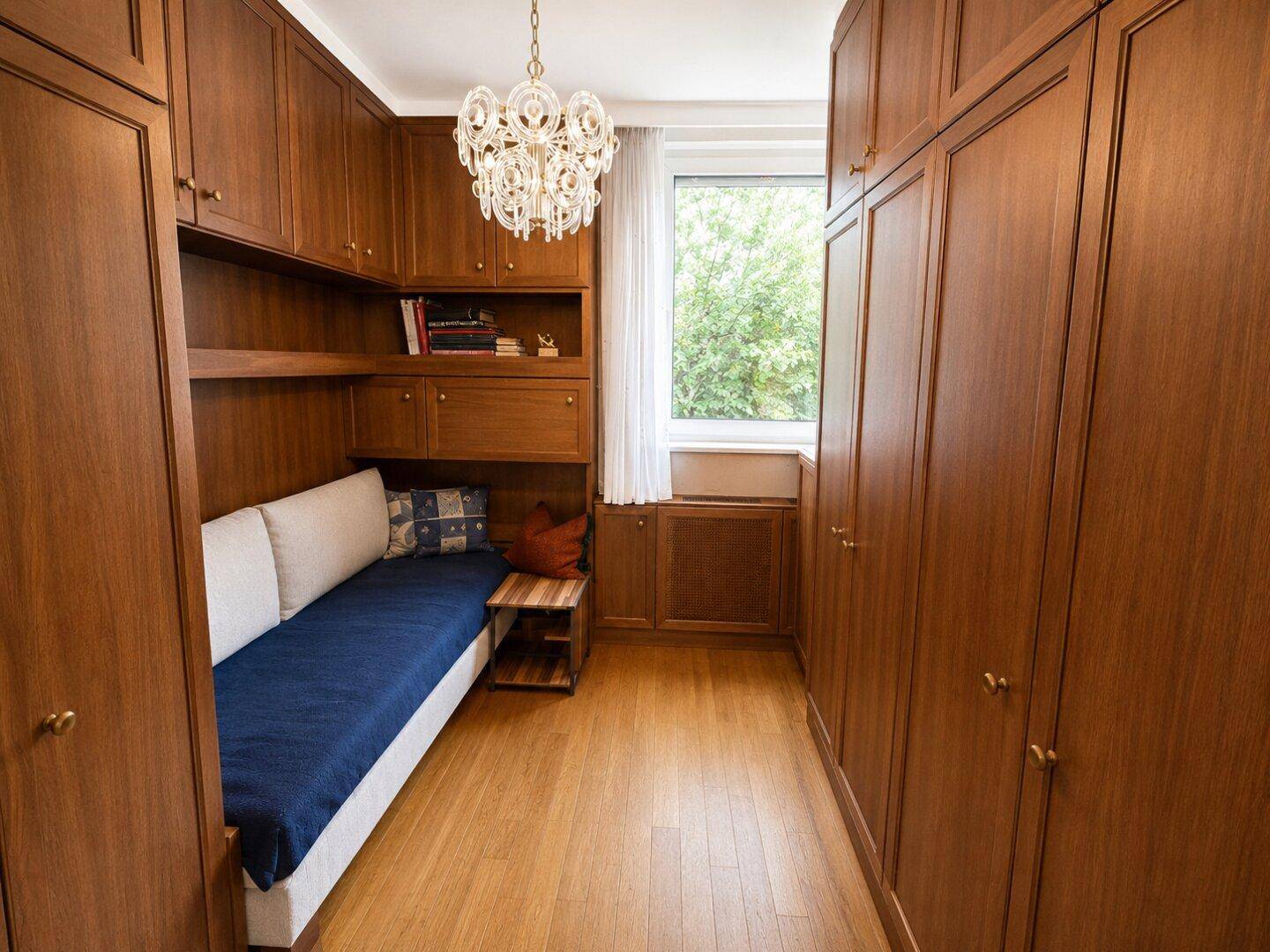 Kleines Zimmer mit Einbauschränken, Holzboden und Blick ins Grüne.