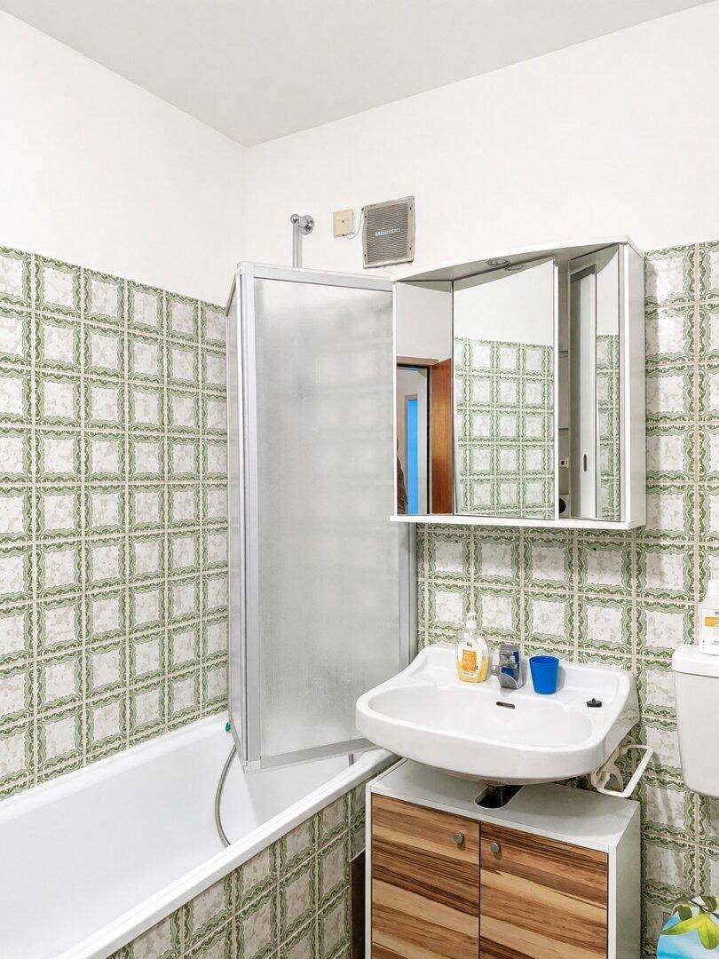 Badezimmer im Stil der 80er Jahre mit grünen Fliesen, Badewanne und Duschabtrennung.